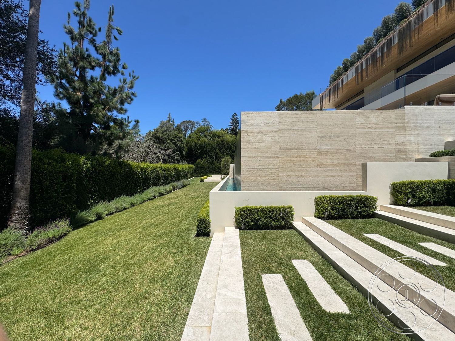 Chalon Estate - exterior, lush greenery, rectangular swimming pool, outdoor living space, contemporary design elements, modern architectural style, tall evergreen trees, landscaped garden area, manicured grass lawn, boxwood shrubs, natural stone wall cladding, cut stone terrace steps, paved terrace flooring, cedar wood balcony