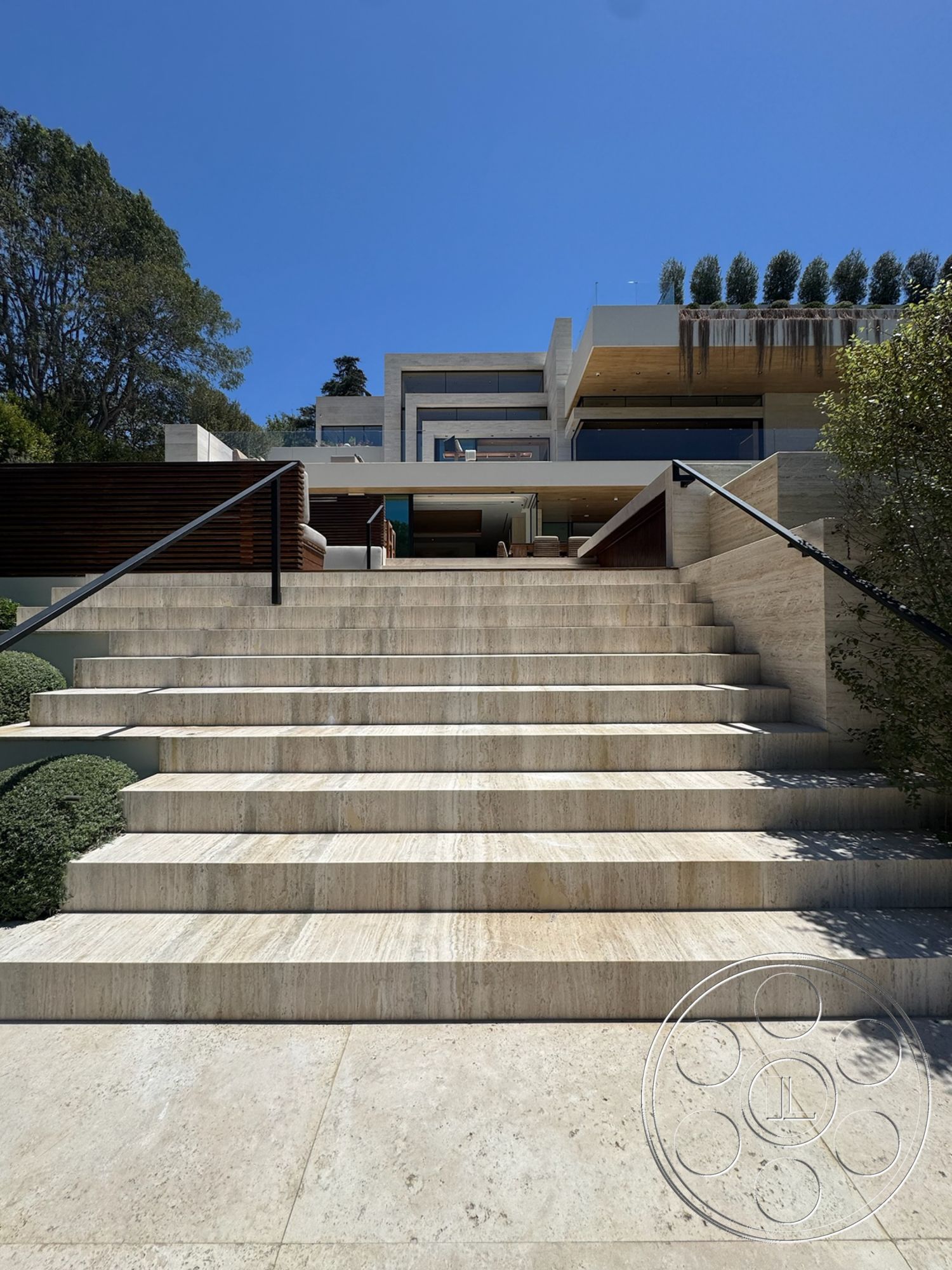 Chalon Estate - modern architectural style, concrete facade, lush greenery backdrop, exterior garden landscaping, metal railing details, wood deck terrace, rectangular building shape, expansive glass windows, travertine stone steps, flat terrazzo patio