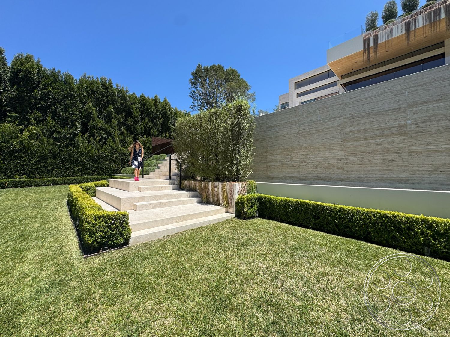 Chalon Estate - large windows, exterior, concrete steps, wood deck, green hedges, tall trees, manicured lawn, symmetrical layout, stone retaining wall, grass landscaping, minimalist garden design, modern architectural details
