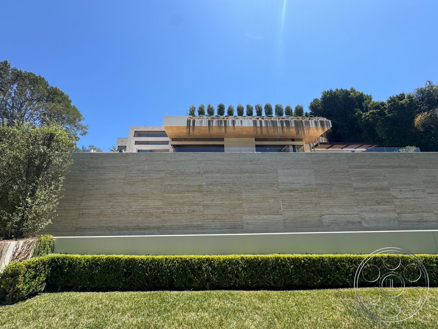 Chalon Estate - exterior, glass railing, landscaped front yard, flat roof design, minimalist architectural style, lush green vegetation, hedge garden borders, stone wall facade, horizontal wooden awning, modern residence