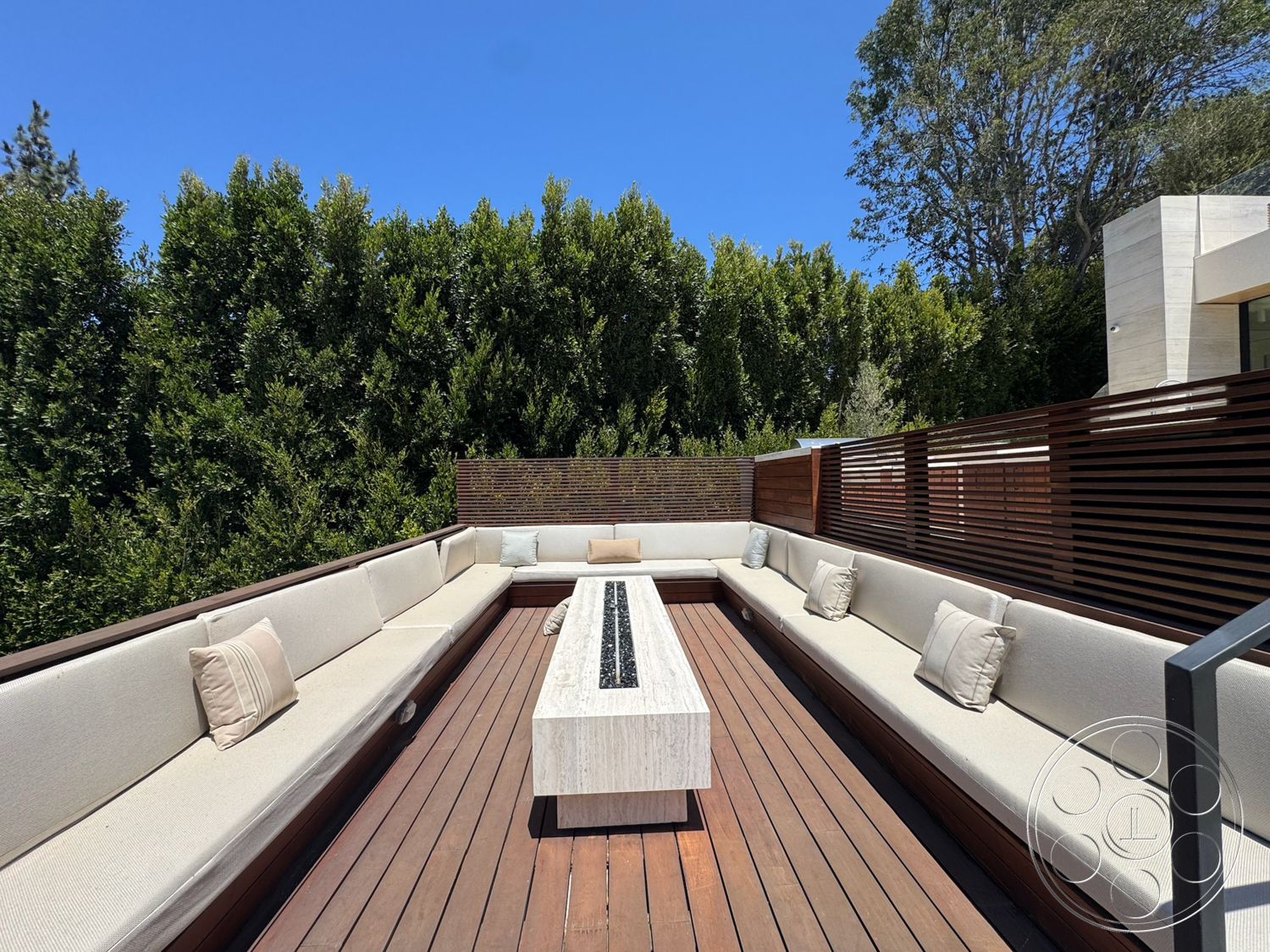 Chalon Estate - exterior, outdoor lounge area, upholstered outdoor seating, lush greenery backdrop, concrete fire pit, wood deck flooring, rectangular seating arrangement, horizontal wooden privacy screen