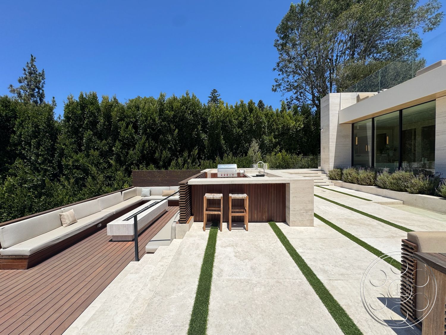 Chalon Estate - exterior, stainless steel grill, minimalist architecture, open air space, modern outdoor seating area, stone patio flooring, rectangular seating arrangement, landscaped garden with hedges, wood deck surface, concrete outdoor kitchen countertop, wood slatted bar structure, linear green grass strips, glass sliders
