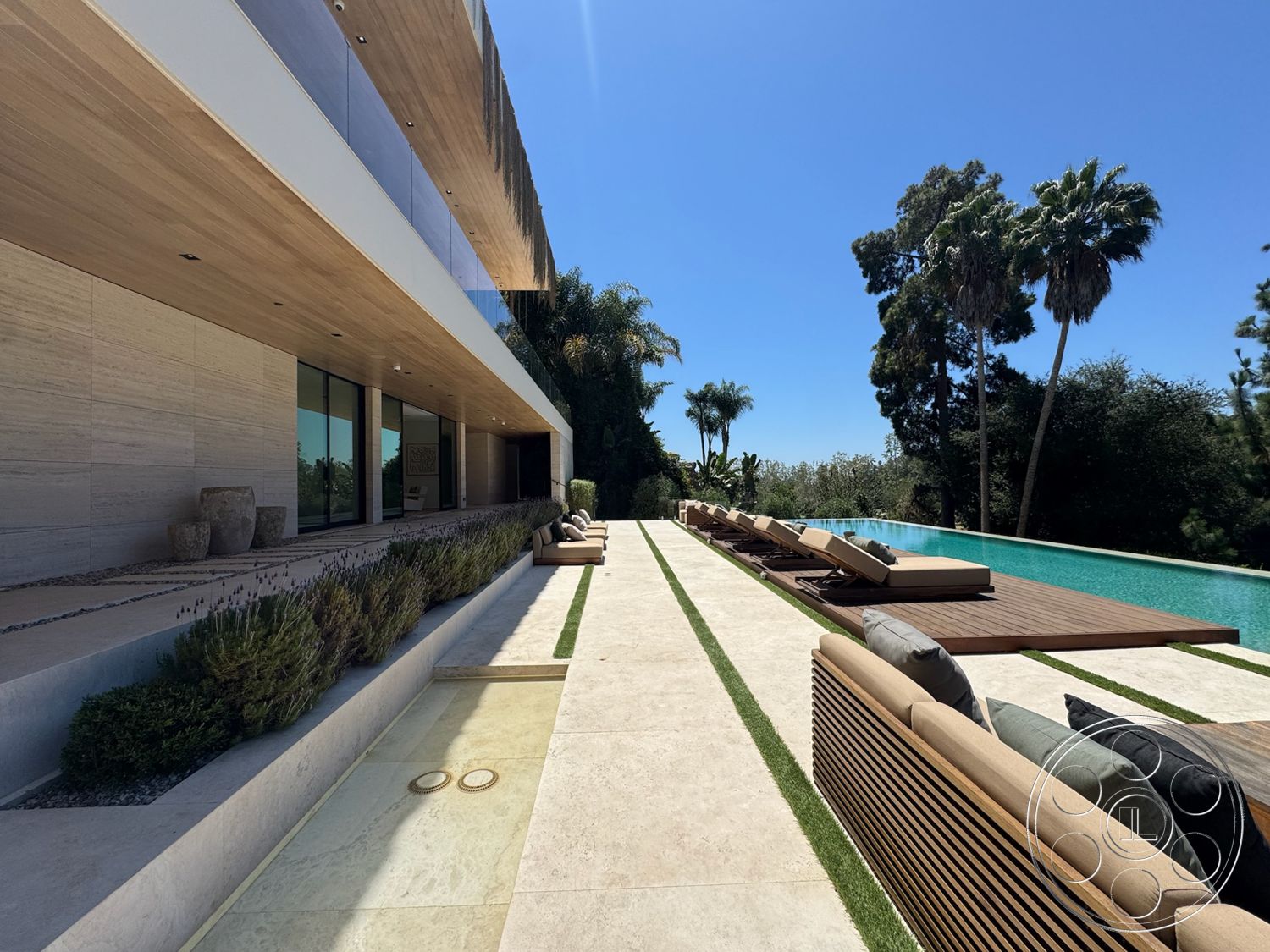 Chalon Estate - modern minimalist design, landscaped garden beds, stone patio flooring, sunny outdoor environment, rectangular infinity pool, urban backyard setting, wood paneling ceiling, outdoor lounge seating area, glass wall openings, low-maintenance greenery, natural stone exterior walls, wooden deck surround