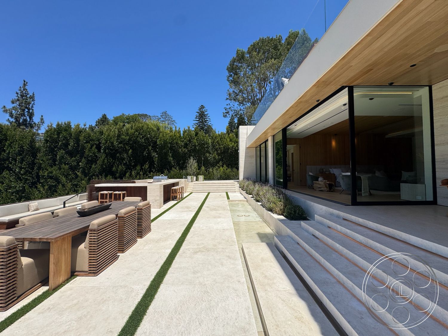 Chalon Estate - exterior, landscaped garden, wood dining table, glass railing, large floor-to-ceiling windows, horizontal wood paneling, natural stone steps, concrete patio flooring, rectangular patio, wood outdoor chairs, stone outline path, striped grass borders
