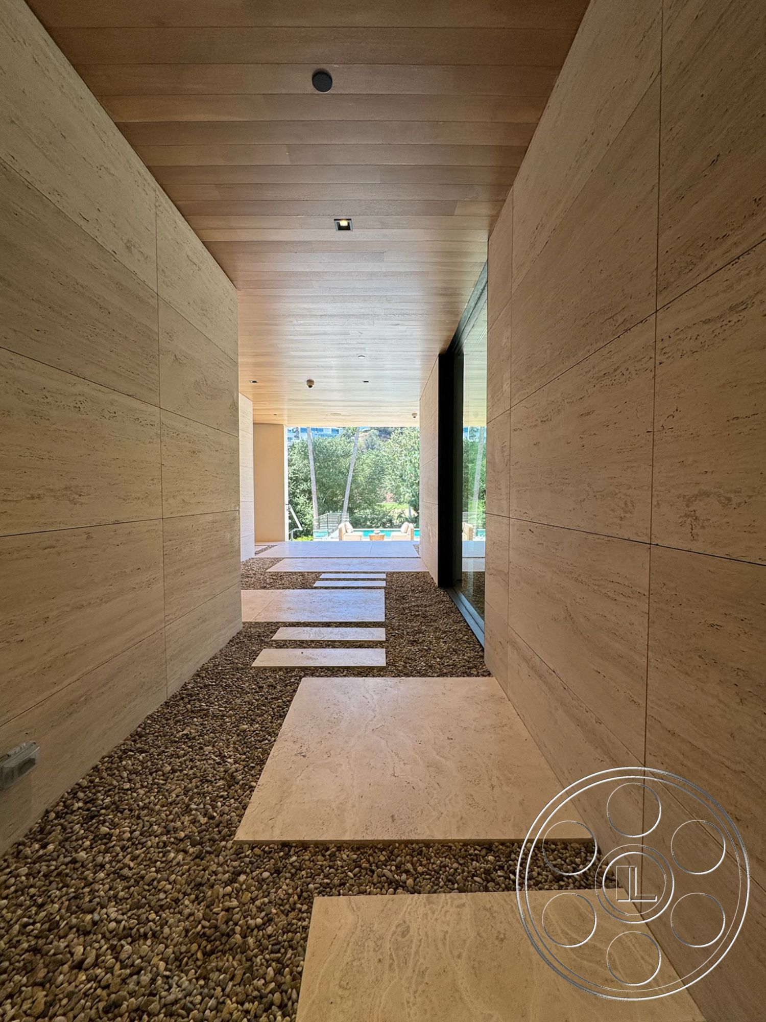 Chalon Estate - wood panel ceiling, large glass windows, open corridor design, natural light-filled hallway, travertine stone walls, pebble stone flooring, rectangular travertine stepping stones