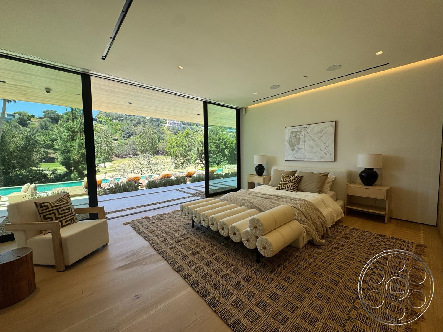 Chalon Estate - textured area rug, large floor-to-ceiling windows, wood accent table, hardwood bedroom floors, neutral painted walls, luxury master bedroom, framed artwork on wall, contemporary bedding, modern bedside tables, glass table lamps, minimalist armchair, open view of landscaped backyard, tray ceiling with recessed lighting