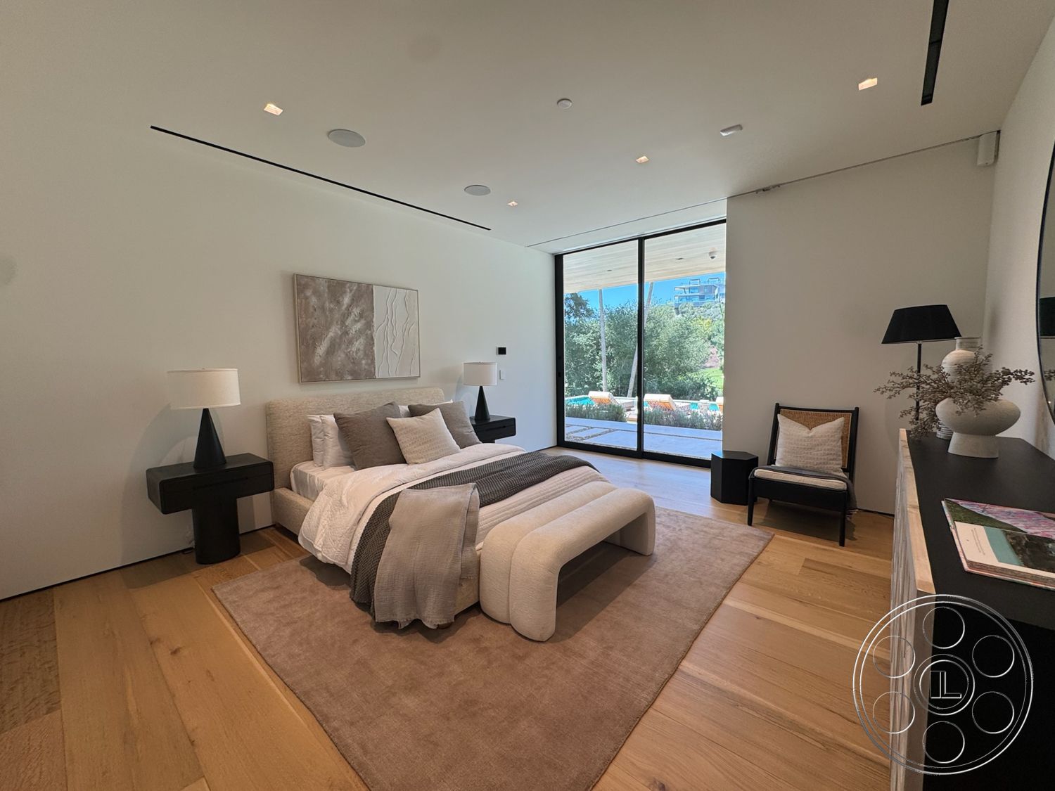 Chalon Estate - minimalist decor, floor-to-ceiling windows, black accent chair, accent art piece, white painted walls, modern upholstered bed, rectangular area rug, wood plank bedroom floors, black side tables, neutral bedding with decorative pillows