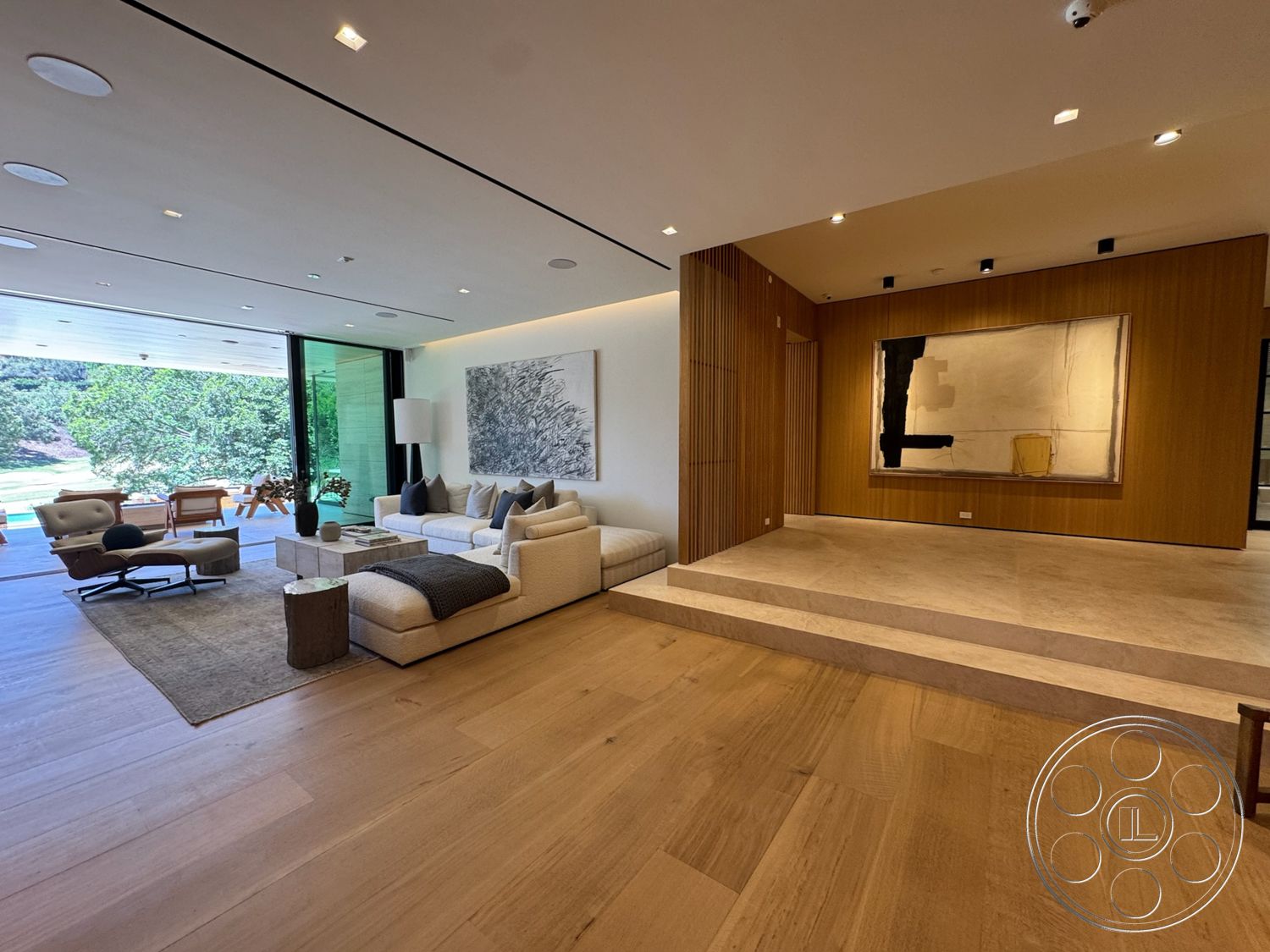 Chalon Estate - neutral color palette, hardwood flooring, textured area rug, open floor plan, modern art wall decor, bright natural lighting, large floor-to-ceiling windows, contemporary living room, minimalist furniture design, glass wall partition, exposed wood panel accent wall, marble steps, seating area with armchairs