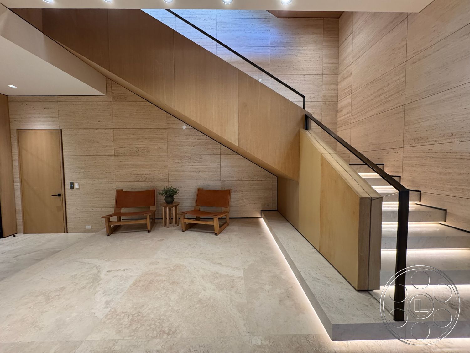 Chalon Estate - modern entryway, polished marble flooring, natural light illumination, minimalist architectural design, wood paneling accent wall, contemporary seating arrangement, black metal stair railings, exposed natural stone wall, light wood stair treads
