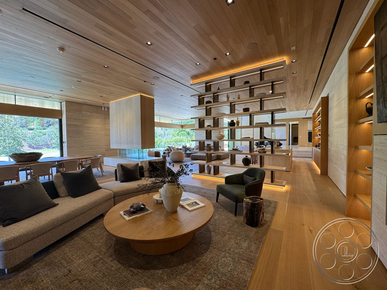 Chalon Estate - neutral area rug, large floor-to-ceiling windows, seamless transition to outdoor space, open-concept living area, minimalist decor style, wood beam ceiling, built-in shelving units, ambient ceiling lighting, modern round coffee table, oak hardwood flooring, contemporary bookshelf design, light wood paneling walls, plush sofa with dark cushions