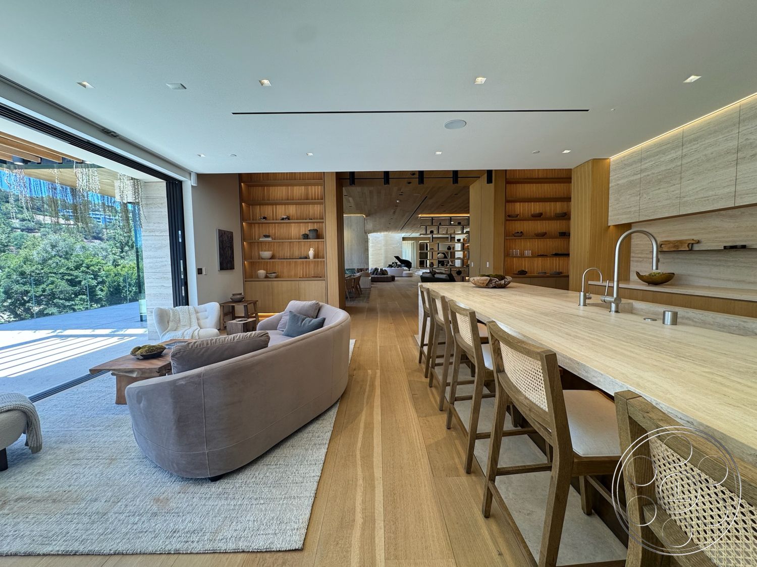 Chalon Estate - minimalist decor, neutral color palette, contemporary design, stone accent wall, cozy seating area, sliding glass doors, built-in shelving, floor-to-ceiling windows, light wood paneling, open-concept layout, circular dining table, woven dining chairs, hardwood living room floors, wood beam ceiling, marble kitchen island, natural light filled space, living area with sectional couch