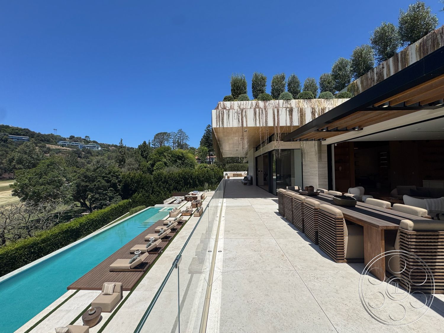 Chalon Estate - exterior, glass sliding doors, wooden dining table, landscaped greenery, rectangular swimming pool, outdoor lounge area, modern architectural style, concrete patio flooring, poolside chaise lounges, overhang roof structure, potted topiary trees, stone perimeter wall, decking area