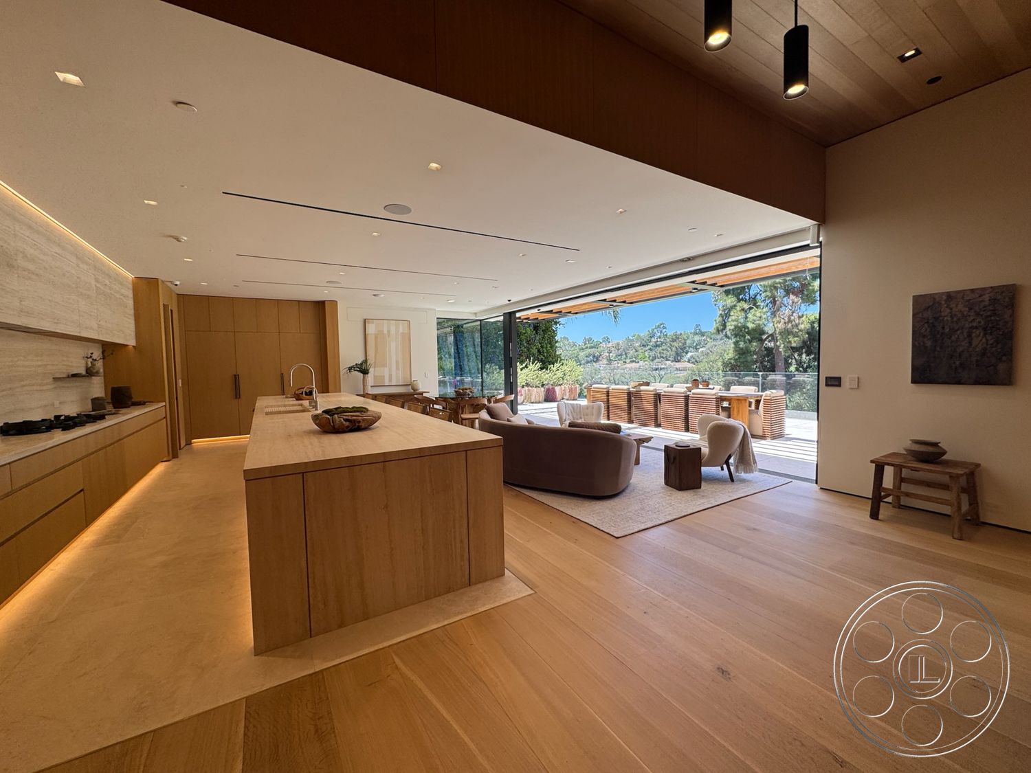 Chalon Estate - neutral color palette, hardwood flooring, large glass sliding doors, open concept layout, modern pendant lighting, light wood cabinetry, textured plaster walls, natural light flooding, minimalist kitchen design, quartz kitchen countertop, lush outdoor landscaping, exterior patio view