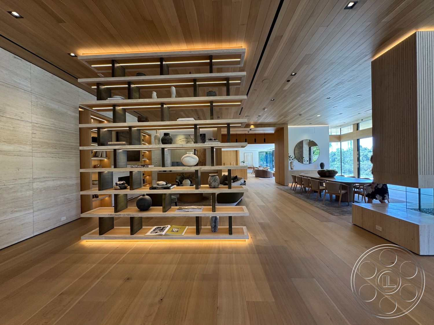 Chalon Estate - neutral color palette, hardwood flooring, stone accent wall, floor-to-ceiling windows, ambient lighting features, minimalist dining area, open concept living area, modern furniture design, oak wood ceiling panels, exposed wooden shelving unit, lighted shelving, decorative round mirror
