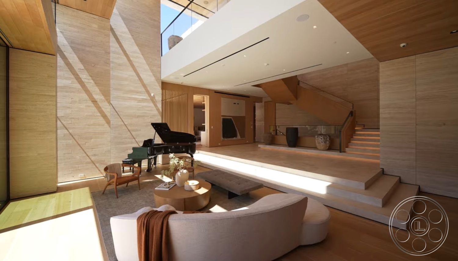 Chalon Estate - open floor plan, modern furniture, circular coffee table, warm wood accents, grand piano, hardwood living room floors, natural light through large windows, wood beam ceiling, glass balcony railing, floating wood staircase, white stone feature wall, plush sofa with throw blanket