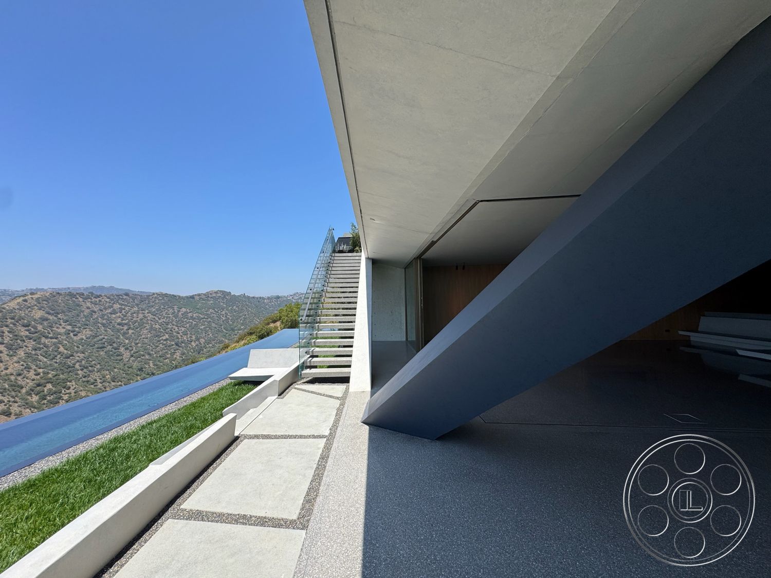 Modern 516 - exterior, sliding glass doors, infinity edge pool, glass railing staircase, grass landscaping, mountain view setting, concrete patio flooring, horizontal concrete slabs, polished concrete steps, angular concrete structure