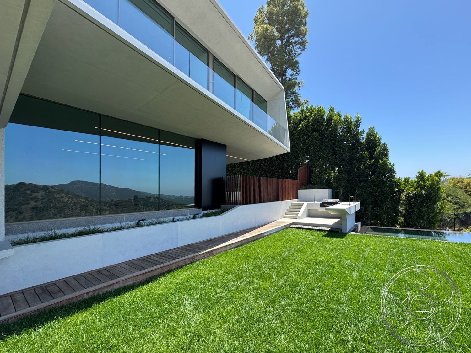 Modern 516 - exterior, landscaped garden, flat roof, sloped terrain, concrete patio, concrete walls, floor-to-ceiling windows, wooden privacy fence, contemporary architectural style, mountain view setting, grass lawn area, wood deck pathway, modern outdoor pool