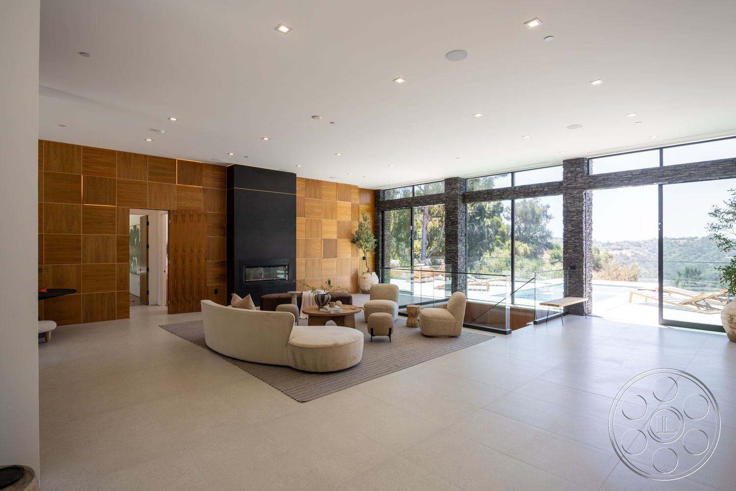 Canyon House - open floor plan, modern aesthetic, minimalist coffee table, large floor-to-ceiling windows, light-colored tile flooring, natural light-filled space, decorative indoor plants, wood panel accent wall, black stone fireplace wall, curved upholstered seating
