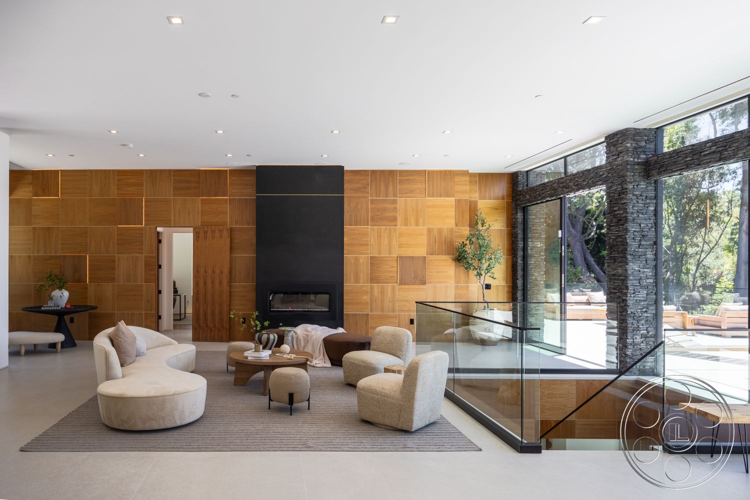 Canyon House - minimalist decor, natural light, round coffee table, large floor-to-ceiling windows, curved sectional sofa, light gray tile flooring, exposed wood paneling accent wall, black stone fireplace wall, black metal and glass stair railing