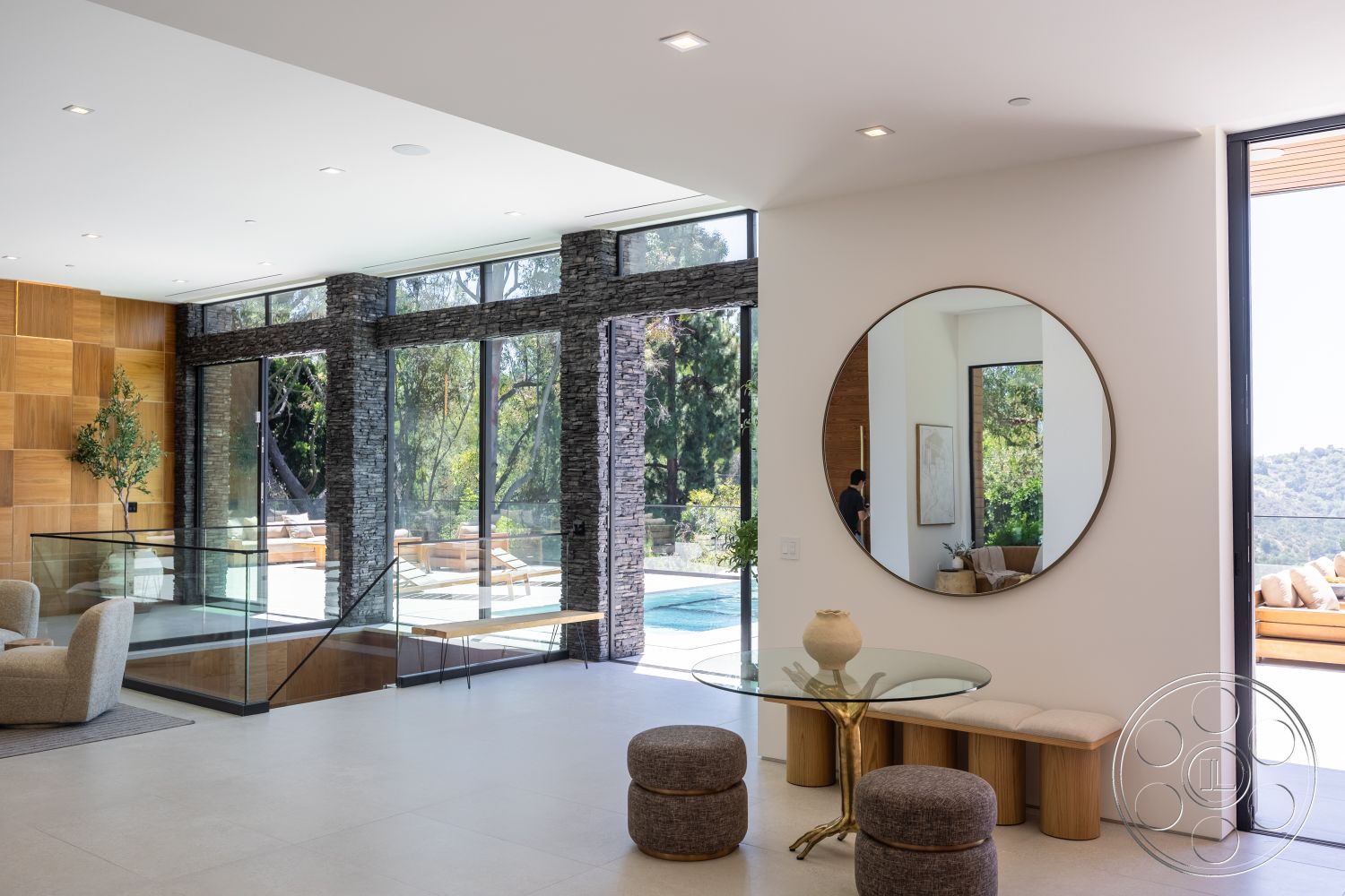 Canyon House - natural lighting, open floor plan, indoor greenery, large floor-to-ceiling windows, glass railing staircase, light-colored tile flooring, modern minimalist design, modern glass dining table, textured wood accent wall, natural stone wall treatment, round mirror wall decor, textured fabric ottomans, view to outdoor patio area
