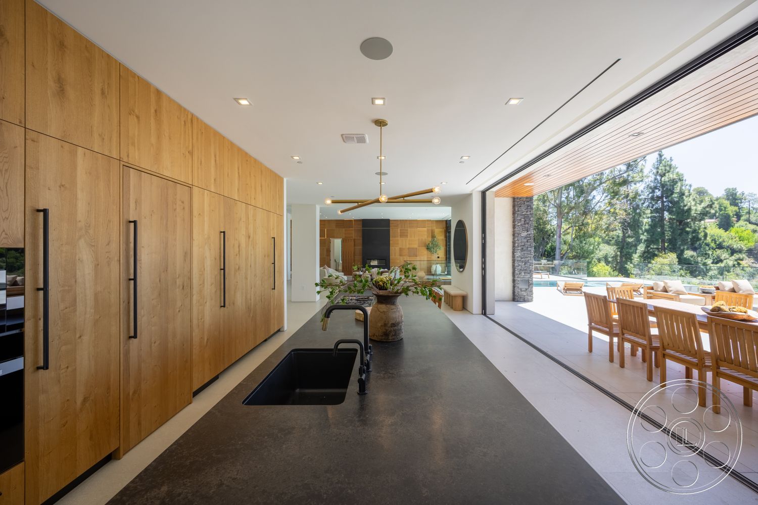 Canyon House - open floor plan, contemporary pendant lighting, polished concrete floors, floor-to-ceiling windows, light wood accents, natural greenery view, seamless indoor-outdoor flow, stone feature wall, wooden dining chairs, recessed ceiling lighting, modern kitchen layout, oversized sliding glass doors, oak kitchen cabinets, black concrete countertop