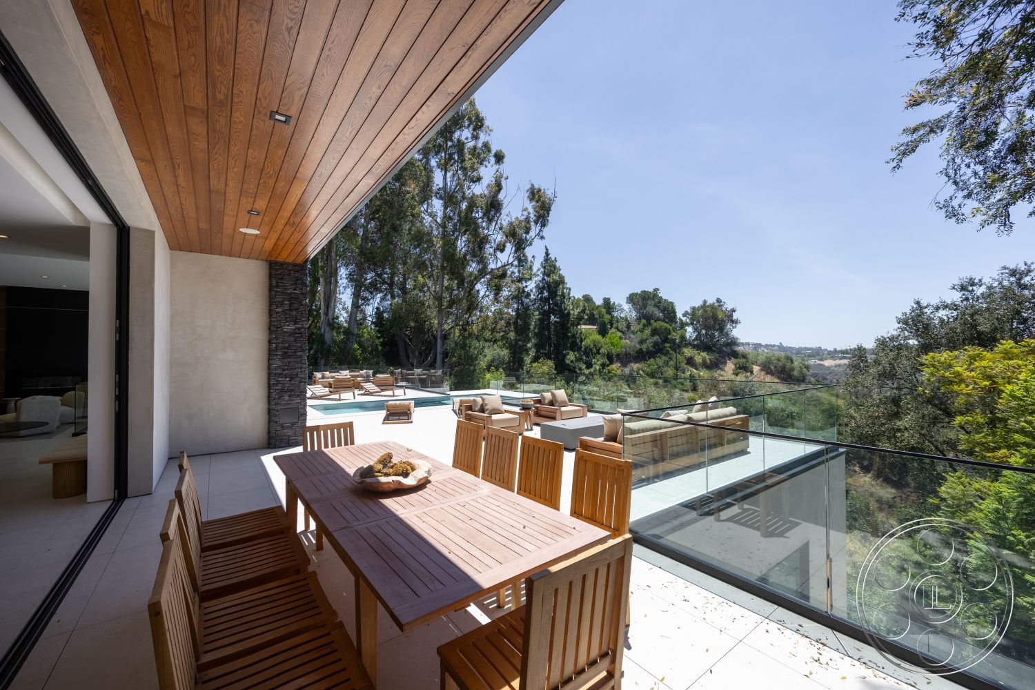 Canyon House - exterior, stone accent wall, wooden dining table, glass railing, landscape view, modern architectural style, concrete patio flooring, wood beam ceiling, lush greenery setting, outdoor lounge seating
