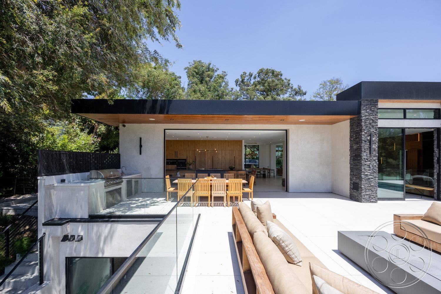 Canyon House - exterior, stone accent wall, glass railing, surrounding greenery, floor-to-ceiling windows, outdoor dining area, modern architectural style, built-in outdoor grill, concrete patio flooring, wood beam ceiling