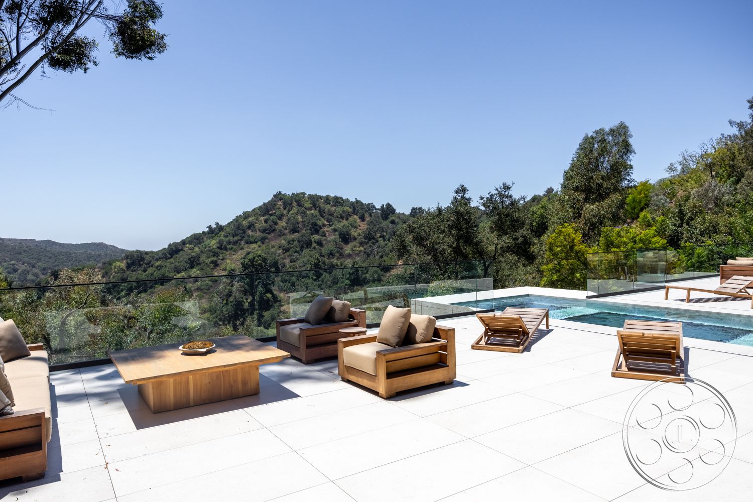 Canyon House - exterior, wooden coffee table, glass railing, rectangular pool, stone pool deck, sunny outdoor setting, wooden outdoor lounge chairs, landscaped hillside view, modern patio flooring
