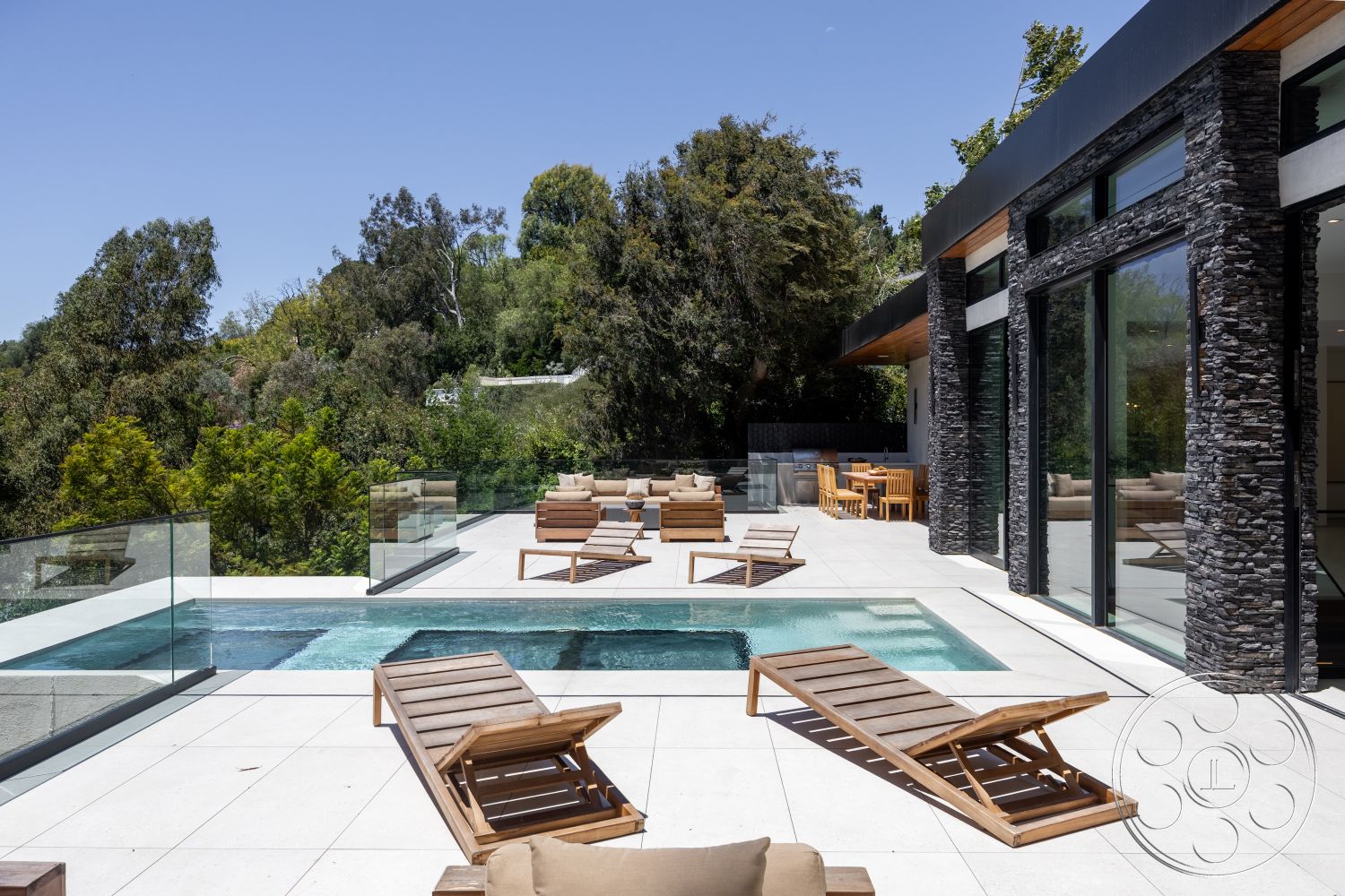 Canyon House - exterior, floor-to-ceiling windows, open-air living space, concrete pool deck, rectangular pool, modern outdoor dining area, landscaped greenery backdrop, wood ceiling overhang, natural stone exterior wall, glass safety railing, hardwood lounge chairs