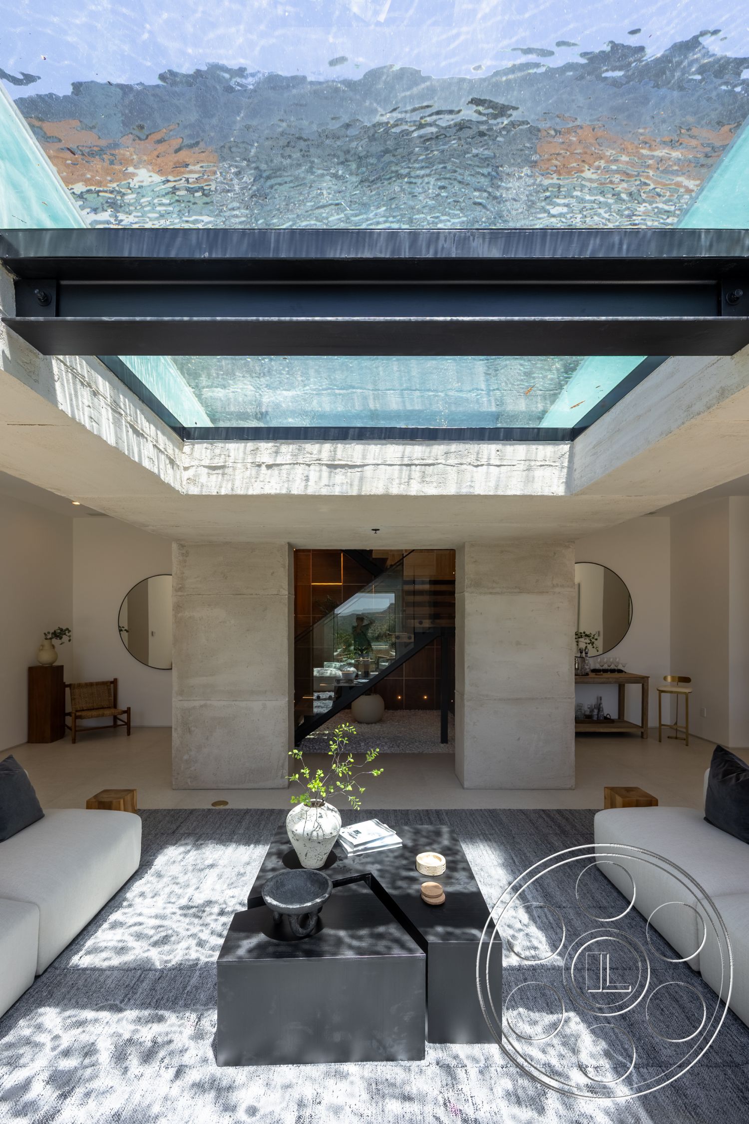 Canyon House - indoor plants, light wood flooring, concrete walls, white upholstered sofa, wooden accent chair, modern architectural style, glass skylight, steel staircase, open living space layout, natural light flooding in, minimalist black coffee table, concrete ceiling with skylight, textured gray area rug, circular wall mirror