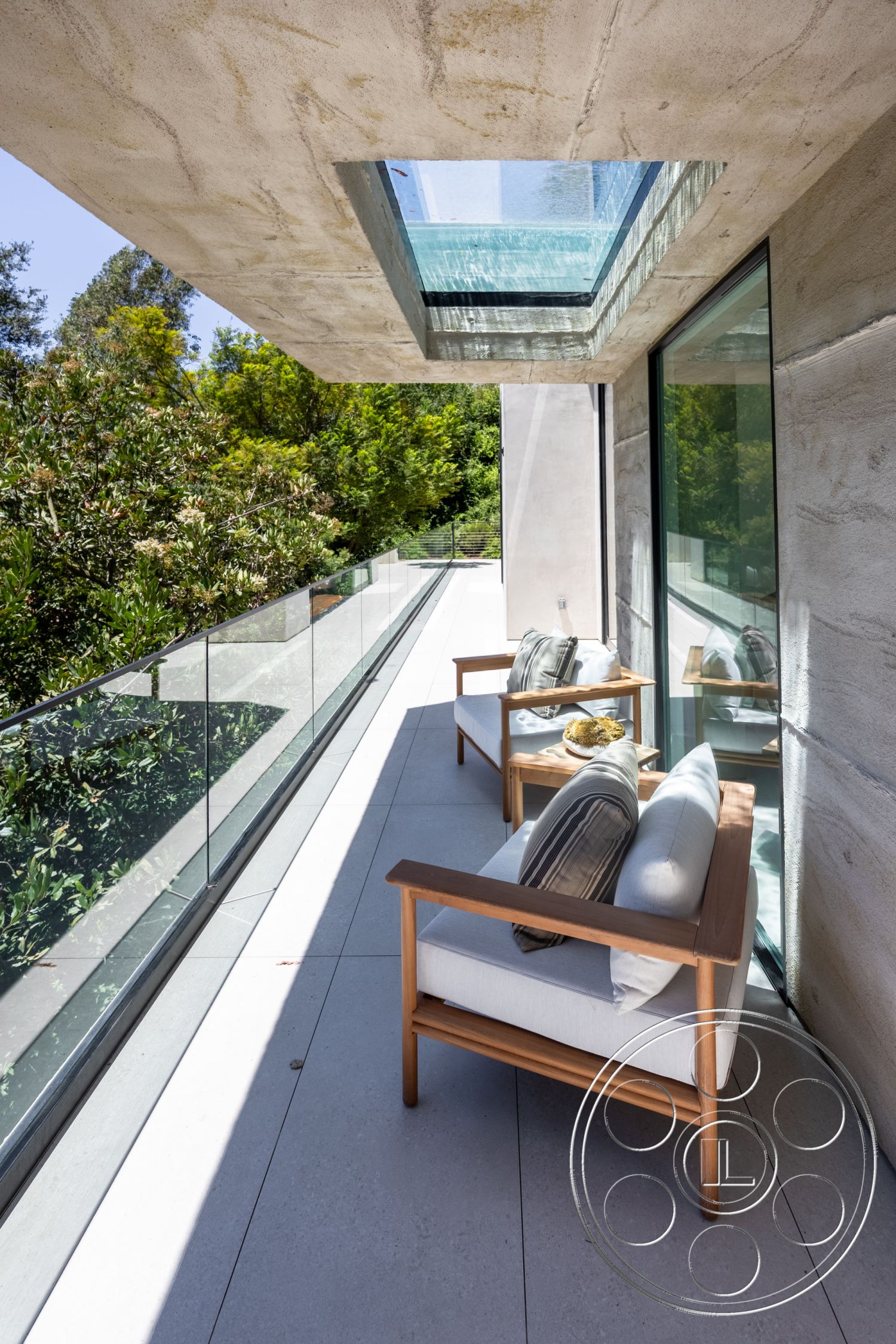 Canyon House - exterior, glass railing, large sliding glass doors, modern outdoor seating, contemporary architectural style, lush greenery setting, skylight feature, concrete balcony ceiling, porcelain patio flooring, wooden chair frames