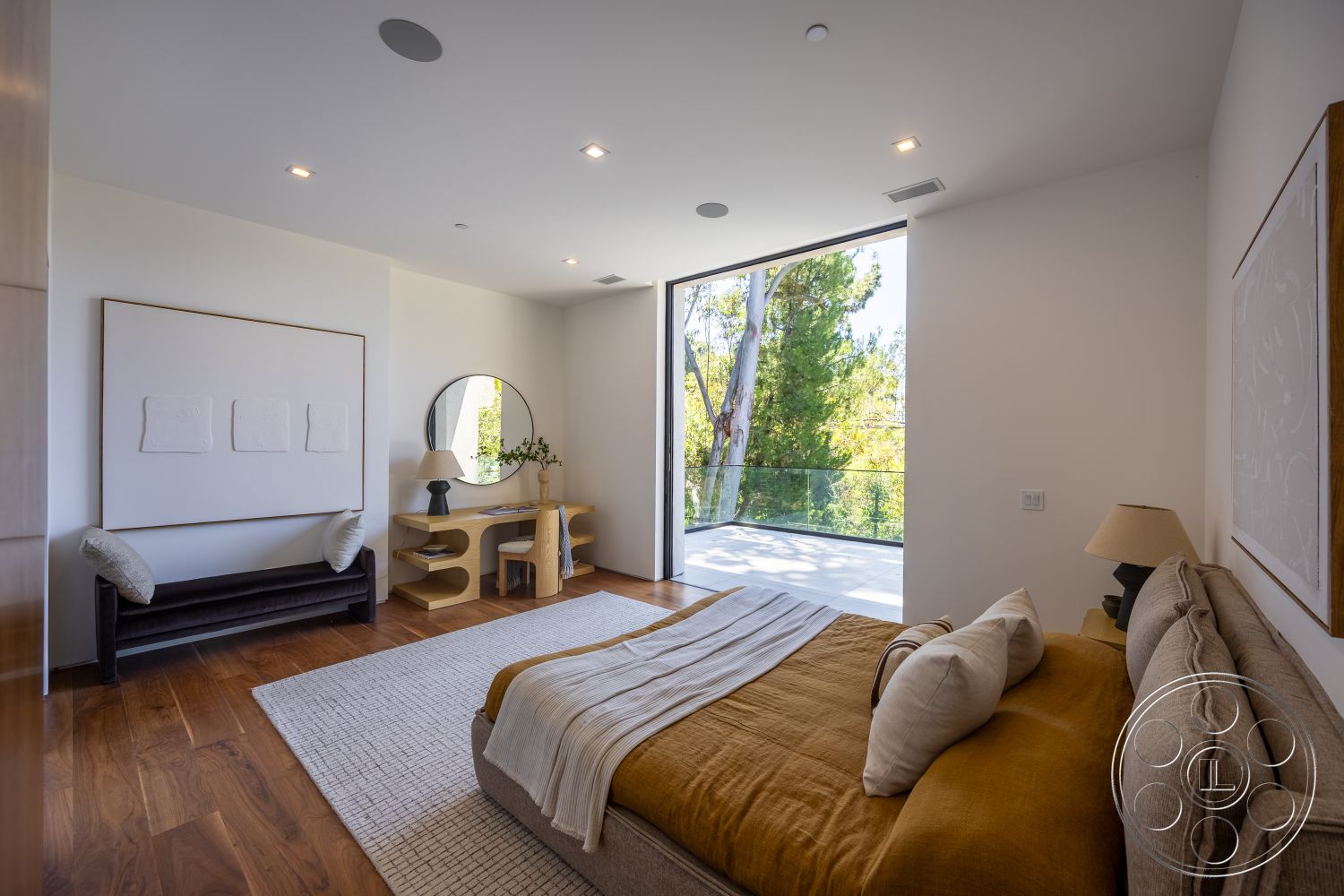 Canyon House - textured area rug, greenery view, floor-to-ceiling windows, interior bedroom, hardwood bedroom floors, white painted walls, glass balcony railing, minimalist art wall decor, modern round mirror, tan upholstered bed, contemporary writing desk