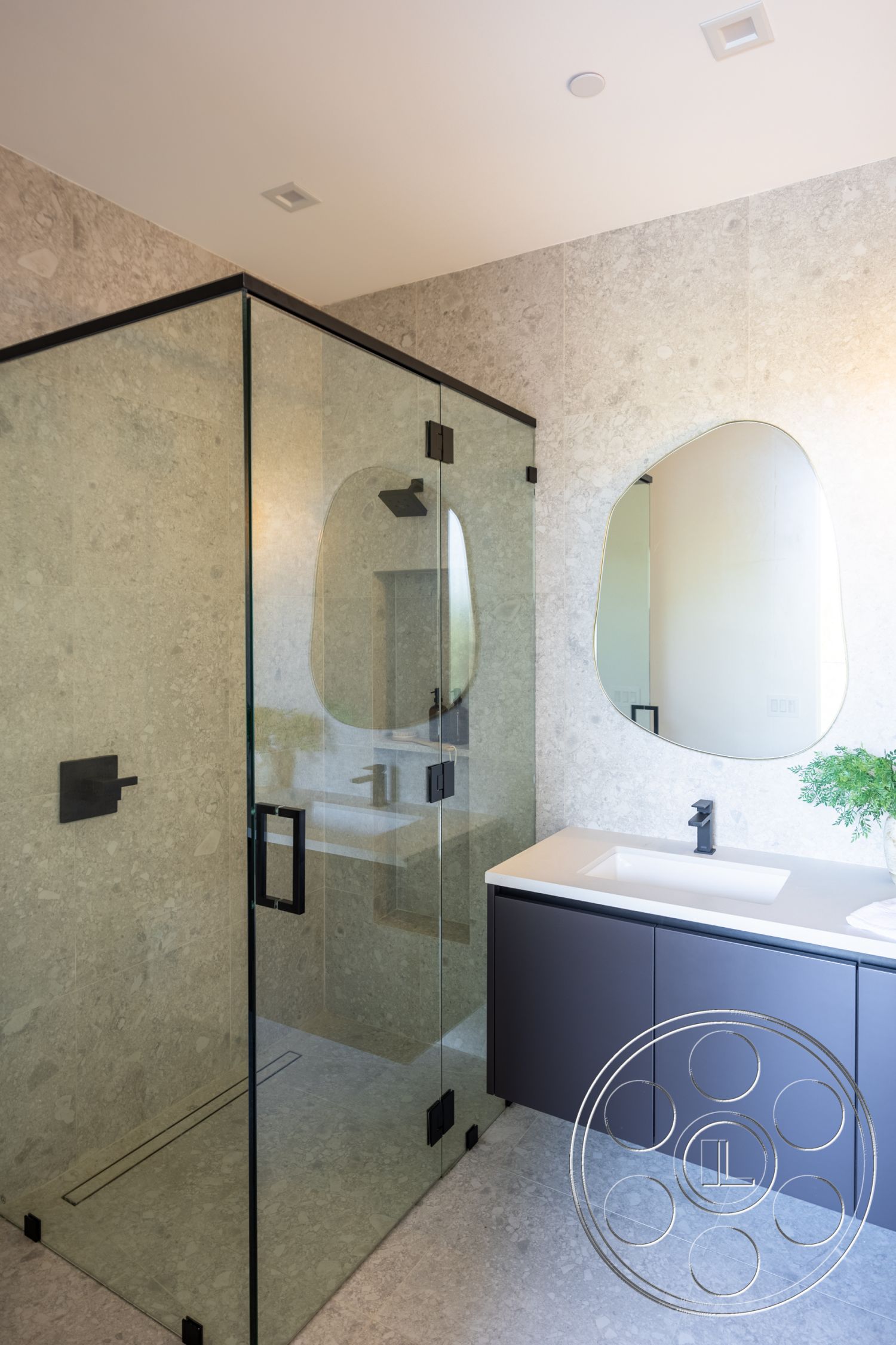 Canyon House - minimalist aesthetic, glass shower enclosure, dark cabinetry, polished stone flooring, oval mirror, recessed ceiling lighting, modern bathroom design, stone shower walls, floating vanity with integrated sink, black faucet fittings