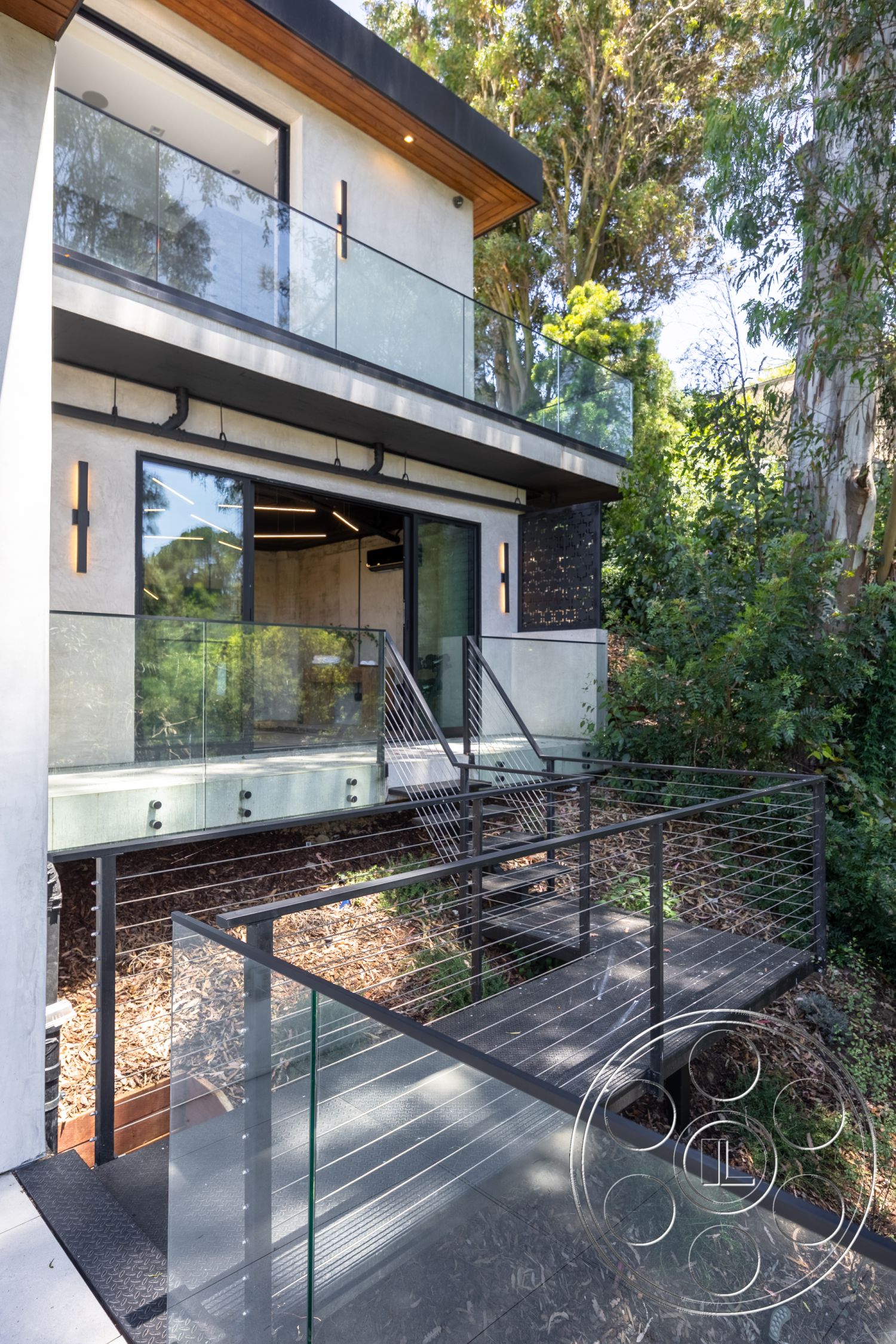 Canyon House - exterior, flat roof, sliding glass doors, concrete walls, modern architectural style, surrounded by greenery, metal staircase, concrete patio flooring, glass balcony railing, open stairwell design, steel cable railing, wood soffit ceiling