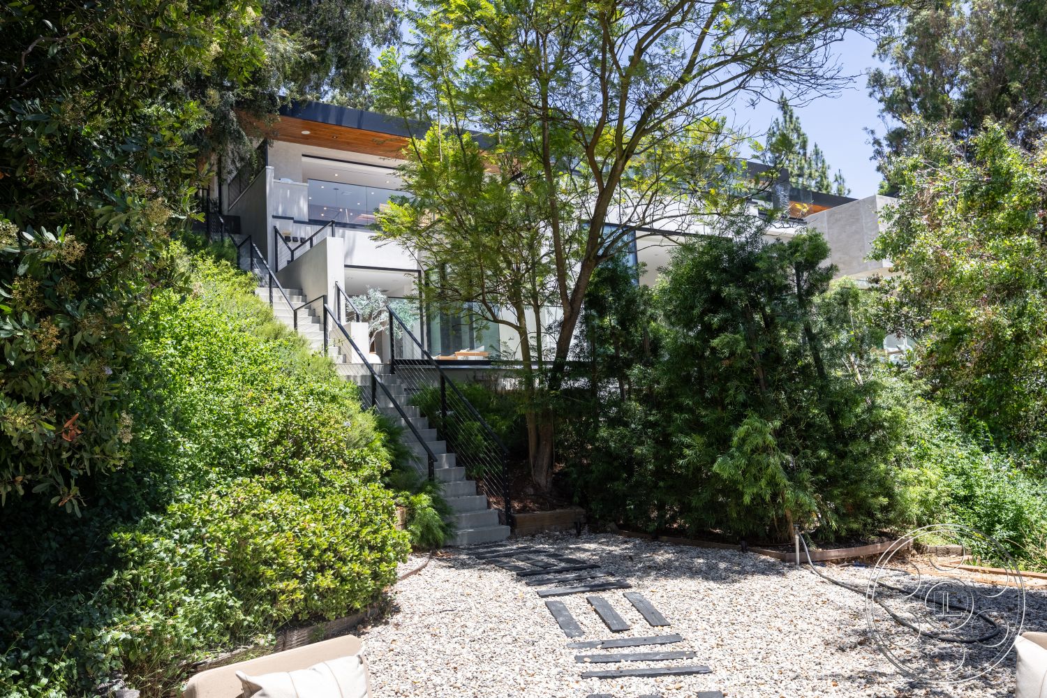 Canyon House - exterior, lush greenery, sloped terrain, metal railing, concrete steps, gravel pathway, modern architectural style, functional outdoor space, tree canopies, floor-to-ceiling glass windows, natural sunlight exposure, multilevel landscaping, wood overhang