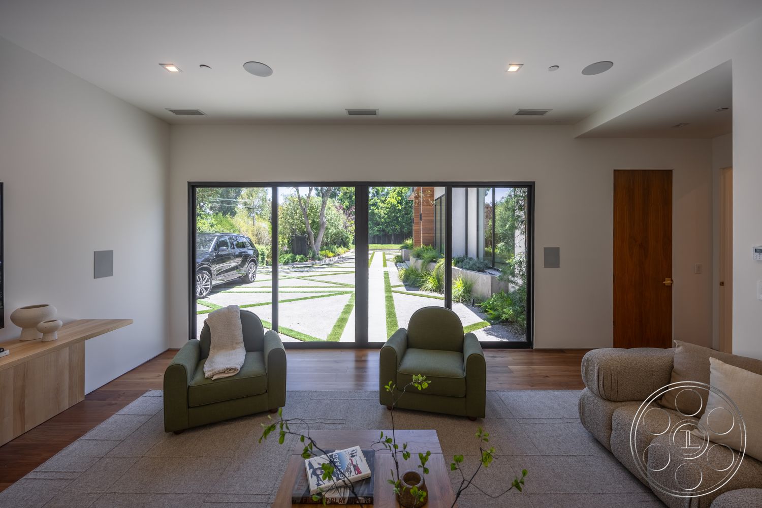 Canyon House - natural light, minimalist design, large glass sliding doors, textured area rug, open floor plan, landscaped garden view, concrete walkway, beige sectional sofa, neutral wall paint, built-in planter boxes, wood plank flooring, modern wooden sideboard, green upholstered armchair