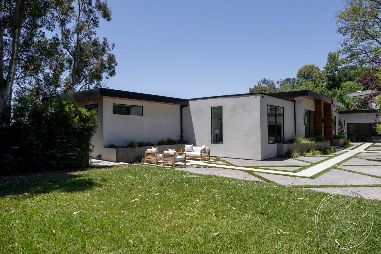 Canyon House - exterior, minimalist design, lush greenery, large glass windows, outdoor seating area, surrounding trees, modern architectural style, concrete driveway, flat roof design, rectangular patio area, linear pathway design, landscaped garden with grass, stucco house walls, wood accents on facade