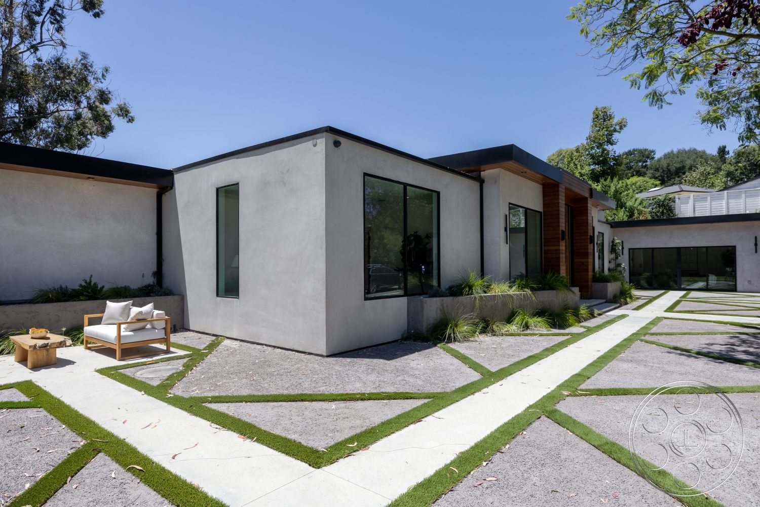Canyon House - exterior, flat roof, minimalist design, outdoor seating area, concrete pathway, outdoor greenery, textured concrete, modern architectural style, stucco walls, gravel driveway, green grass strips, large rectangular windows, landscaped planter beds, wood accent paneling, angular building shapes