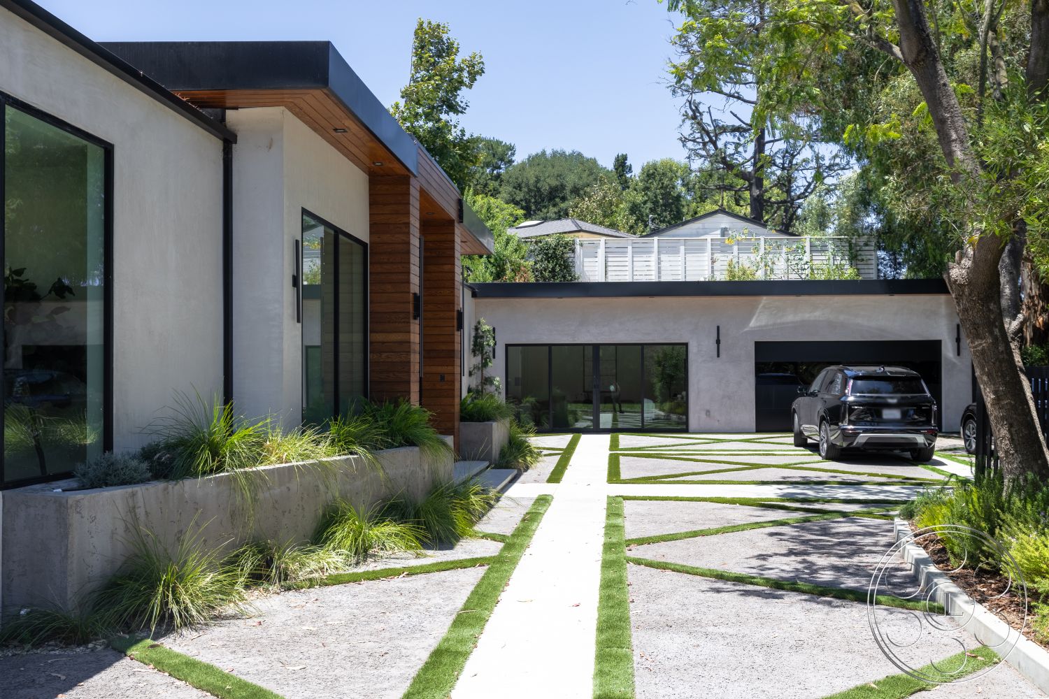 Canyon House - exterior, concrete driveway, modern garage door, flat roof design, landscaped garden beds, minimalist architectural style, large black-framed windows, concrete planter wall, light gray stucco walls, natural wood siding accents, striped grass detailing, native shrubs and grasses