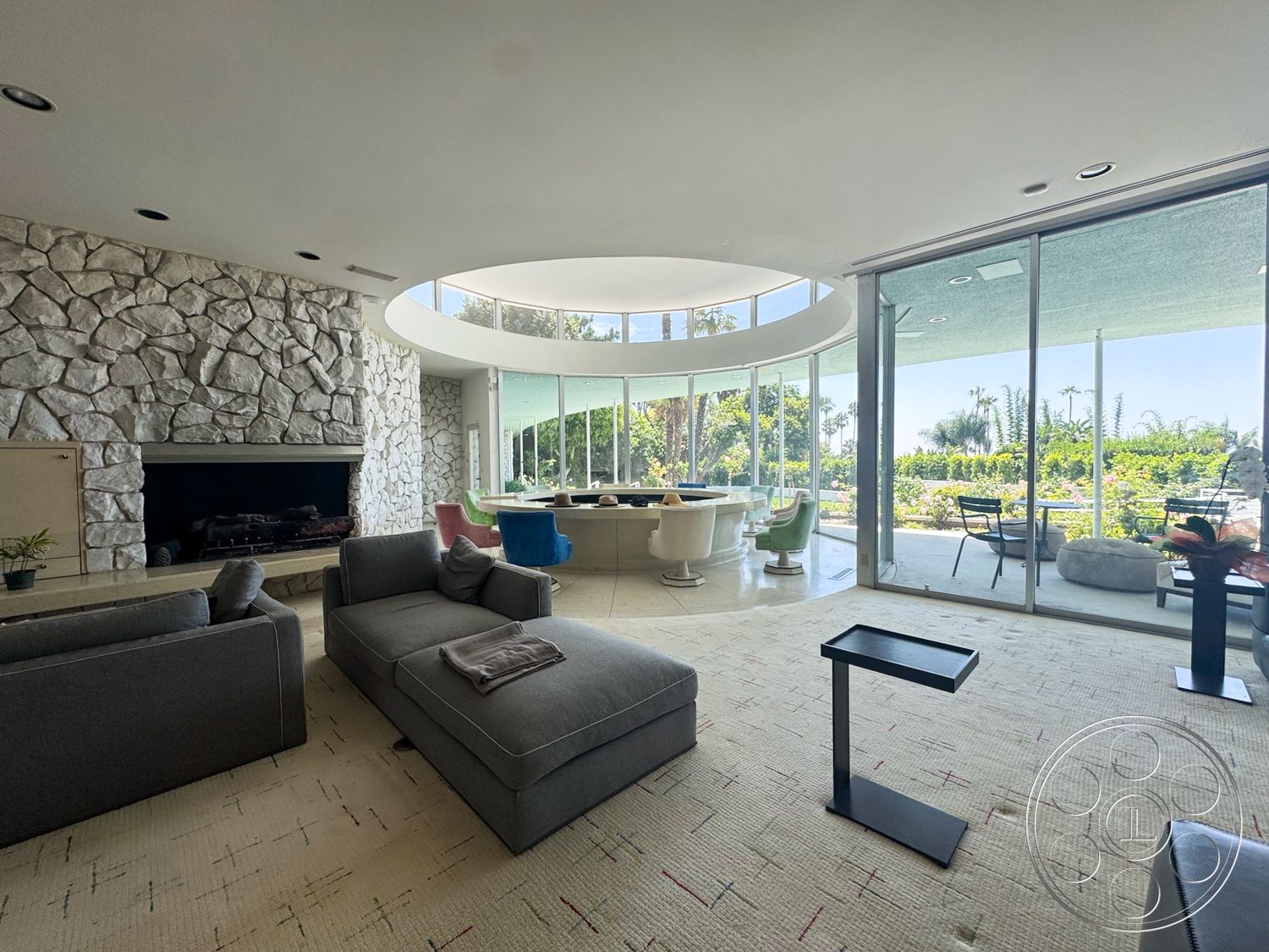 MCM 28 - textured area rug, open floor plan, modern furniture, suburban setting, floor-to-ceiling windows, bright and airy atmosphere, sculptural decor, stone fireplace wall, exposed stone accent wall, palm garden view, stylish lounge seating, circular skylight, round ceiling, contemporary glass dining table