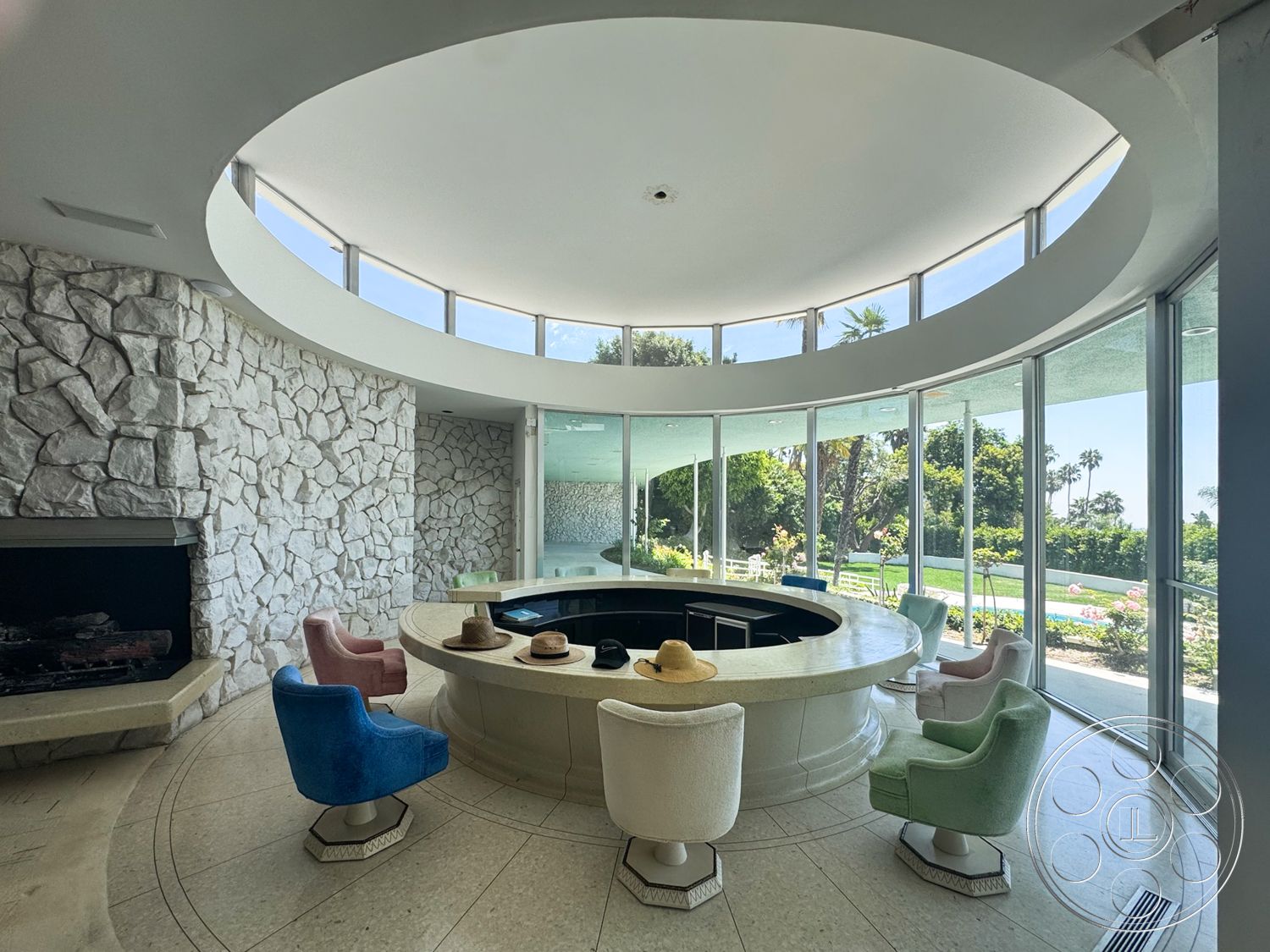 MCM 28 - natural light, open layout, floor-to-ceiling windows, modern architectural style, marble flooring, stone feature wall, mid-century modern design, curved ceiling design, surrounding garden view, colorful upholstered chairs, circular kitchen island, exposed stone fireplace