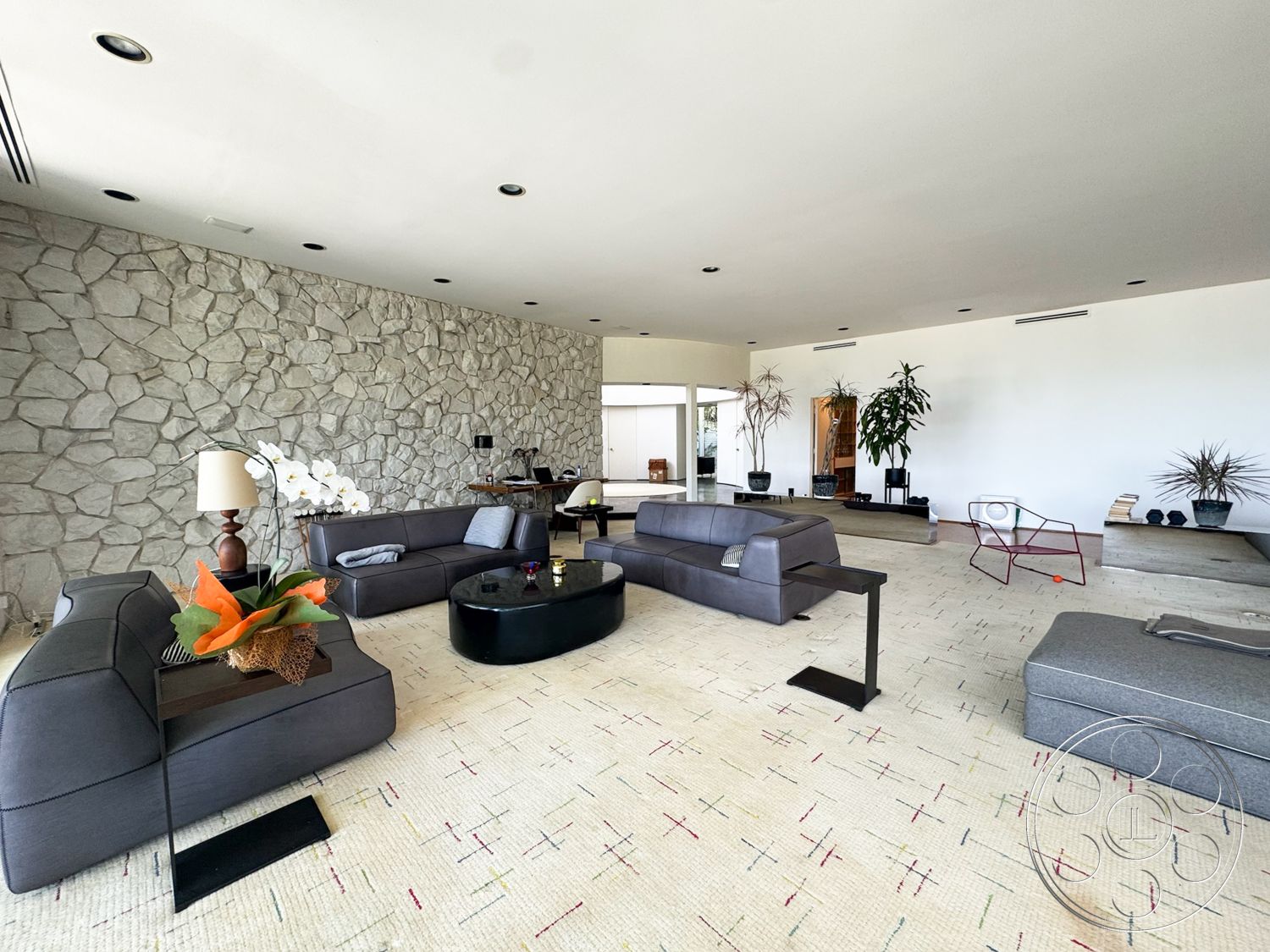 MCM 28 - minimalist decor, open floor plan, modern coffee table, seating area, floor-to-ceiling windows, textured wall treatments, mid-century modern style, stone feature wall, wooden accent table, recessed ceiling lights, contemporary furniture design, natural light illumination, decorative indoor plants, gray leather sectional sofa, flat woven area rug