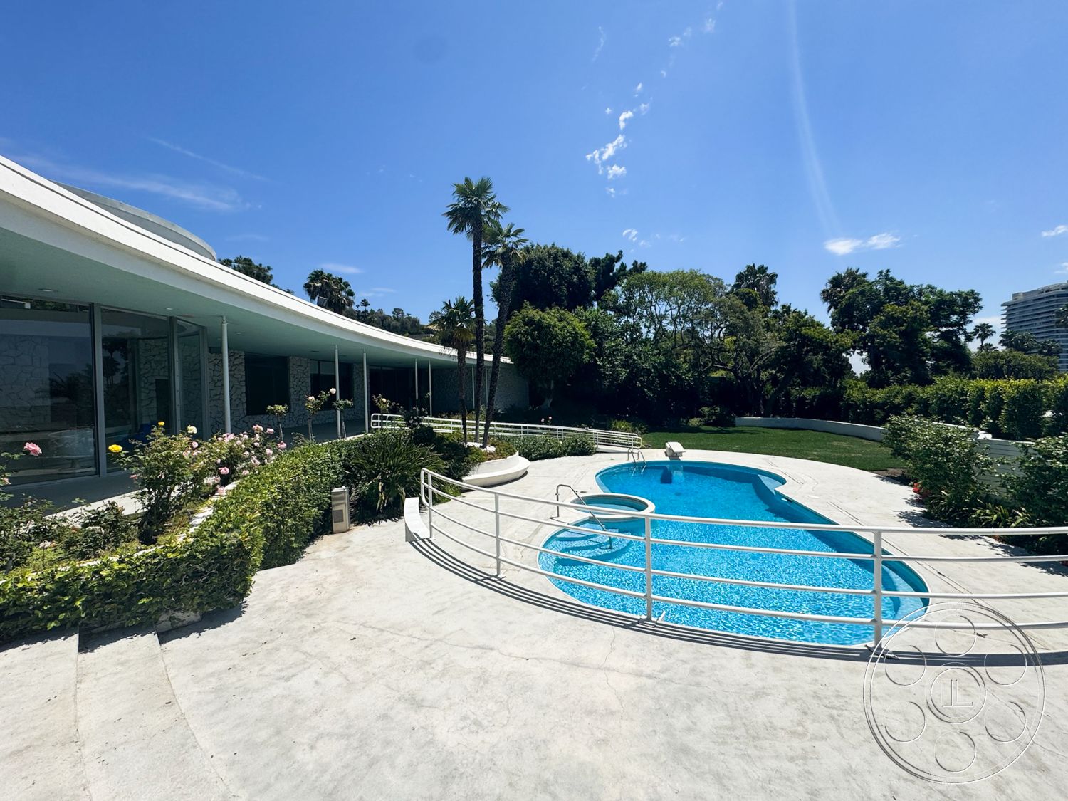 MCM 28 - exterior, palm trees, glass windows, modern architectural style, blue sky, curved roof design, oval pool, lush garden setting, concrete patio floor, landscaped bushes, white metal railings