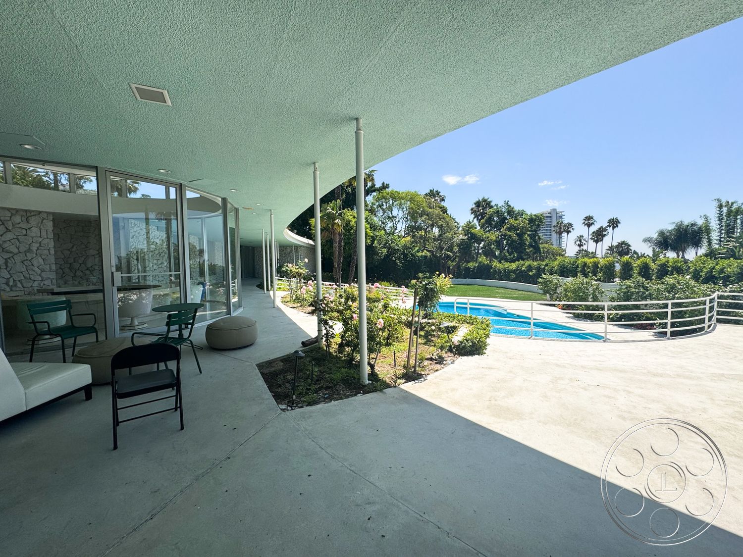 MCM 28 - exterior, stone accent wall, glass sliding doors, outdoor seating area, metal railing, rectangular swimming pool, palm tree view, concrete patio floor, landscape garden setting, curved roof overhang