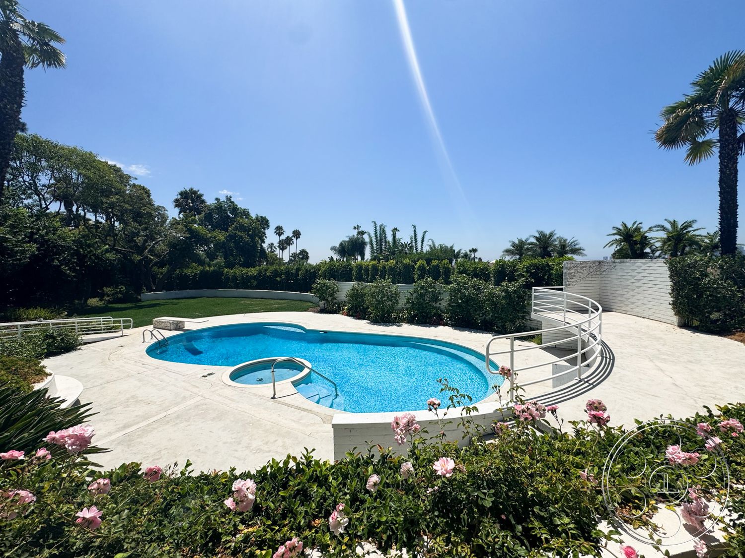 MCM 28 - exterior, palm trees, concrete pool deck, white brick wall, oval swimming pool, landscaped garden area, lush greenery setting, sunny outdoor environment, flowering rose bushes, white pool railing