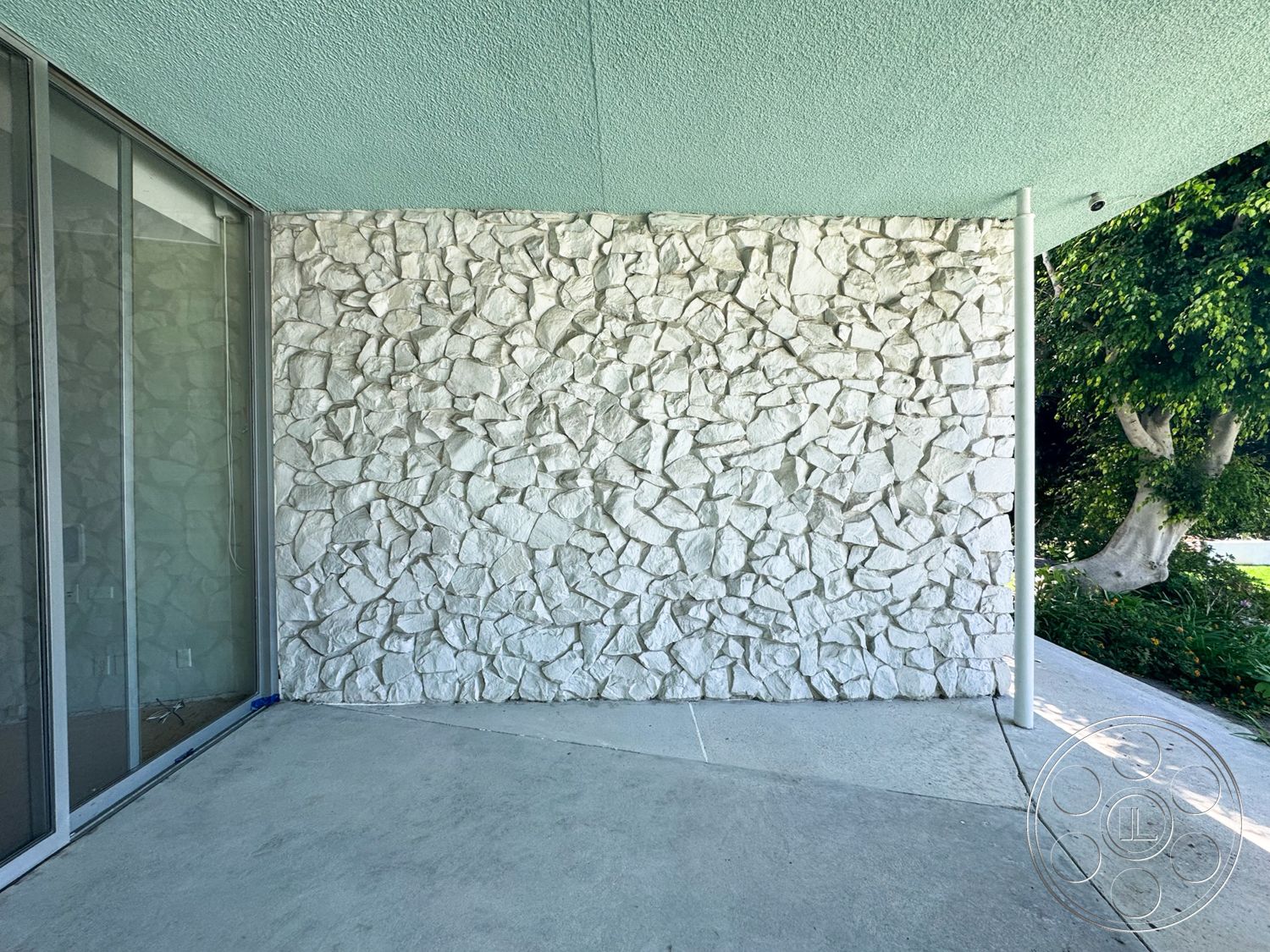 MCM 28 - exterior, glass sliding doors, surrounding greenery, outdoor living space, modern architectural style, exposed stone feature wall, concrete floor patio, roughly hewn stone cladding, horizontal ceiling with textured finish