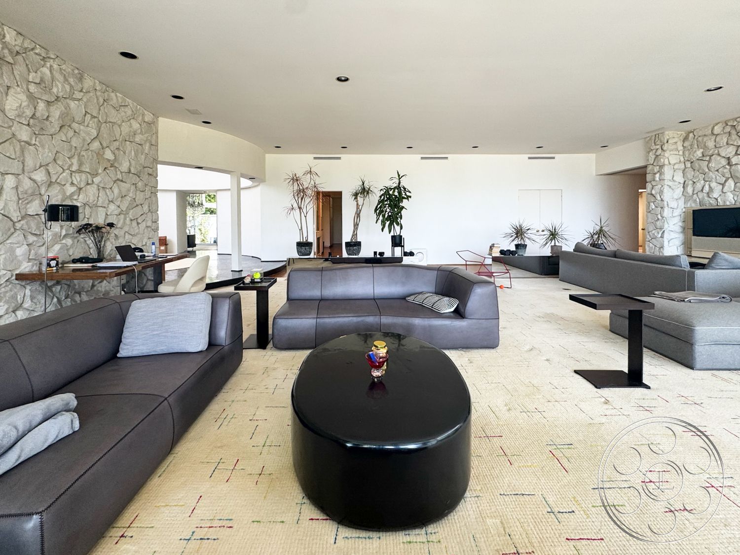 MCM 28 - contemporary furniture, floor-to-ceiling windows, open concept living space, modern minimalist design, neutral painted walls, potted indoor plants, exposed stone feature wall, light-colored area rug, dark leather sectional sofa, black oval coffee table, light wood accent table