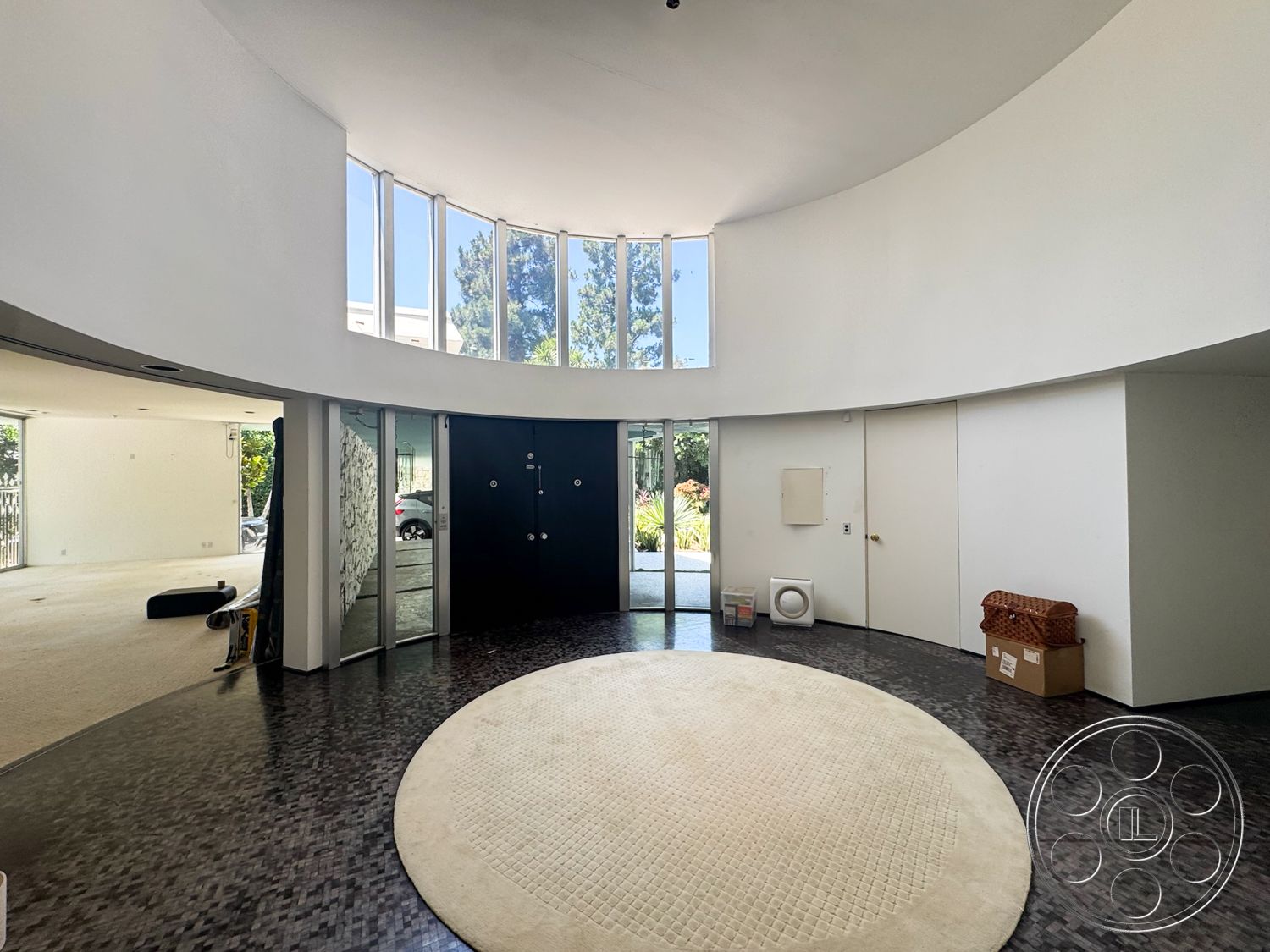 MCM 28 - minimalist decor, open floor plan, transom windows, floor-to-ceiling windows, geometric shapes, contemporary design elements, polished stone flooring, dark wood paneling, circular area rug, curved walls, white painted walls, natural light abundance, round ceiling, modern double doors