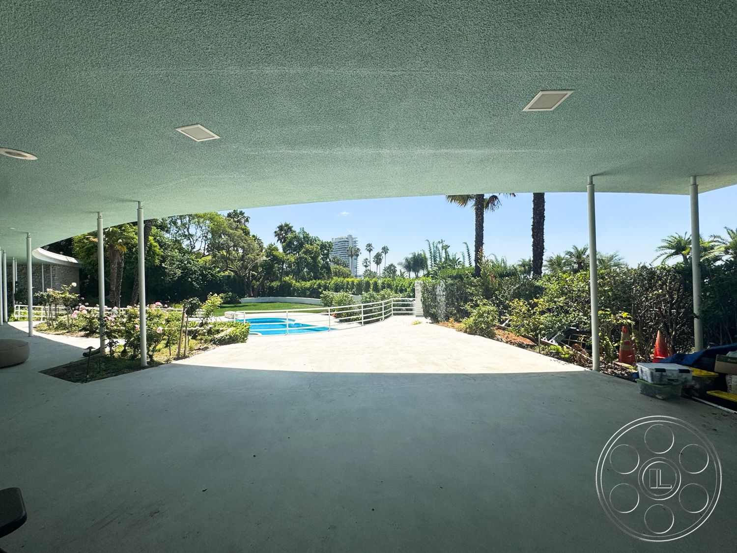 MCM 28 - exterior, palm trees, rectangular swimming pool, modern architectural style, lush tropical landscaping, open-air patio, concrete patio floor, glass fence surrounding pool area, garden rose bushes, pebble stone pathway, overhead roof with recessed lighting