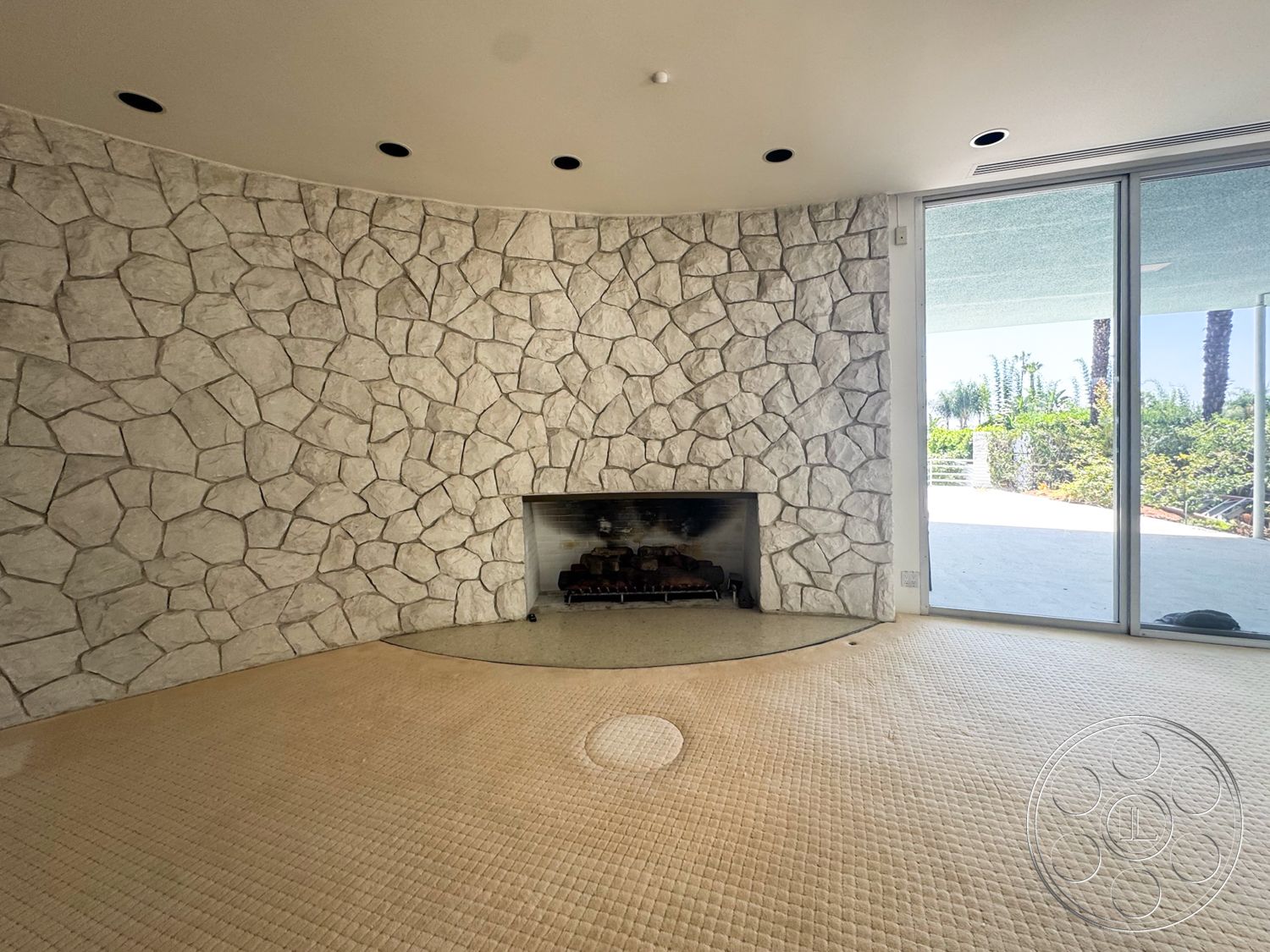 MCM 28 - large glass sliding doors, curved wall design, recessed ceiling lights, suburban backyard view, textured stone feature wall, round stone fireplace surround, tan carpet flooring
